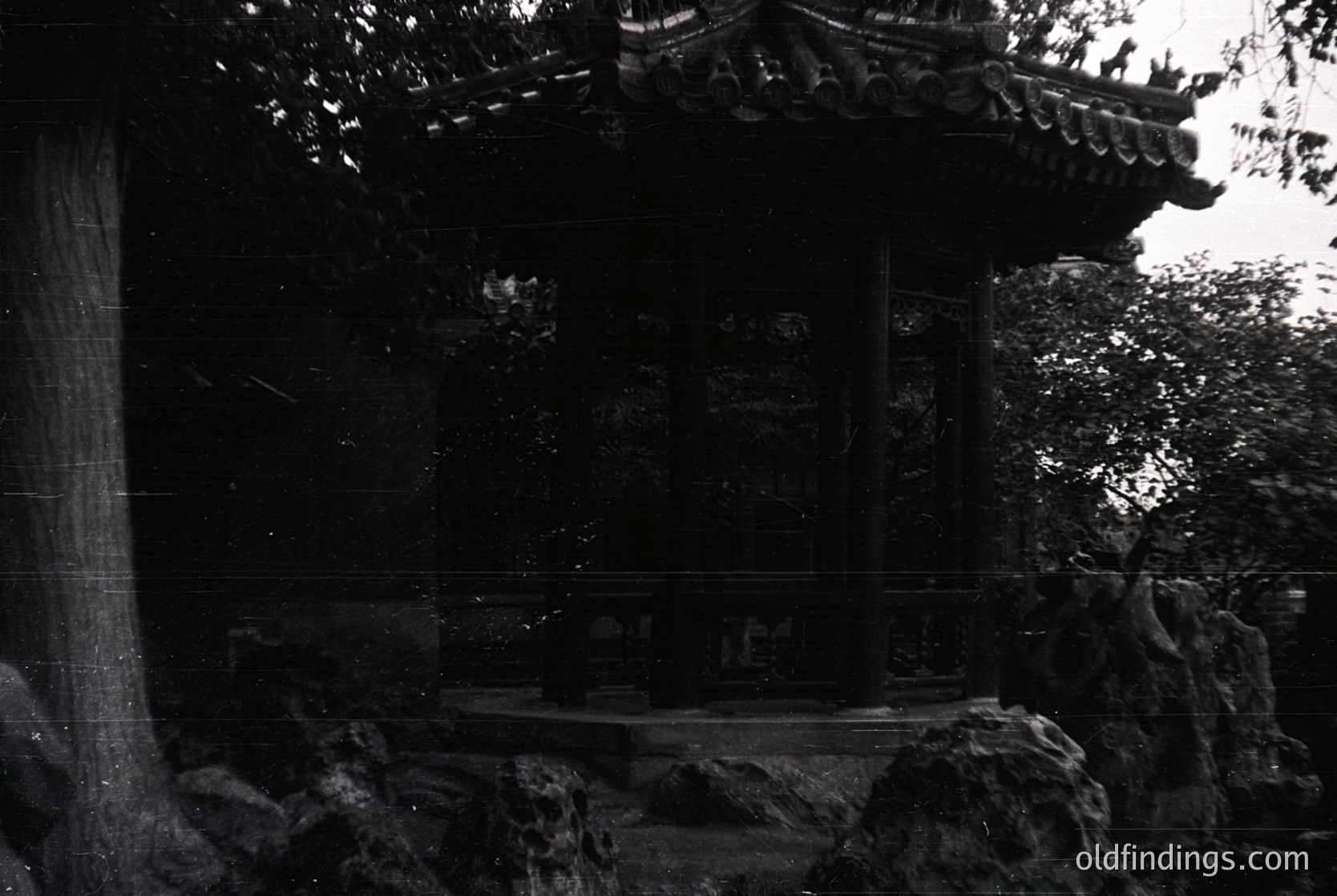 Classic East Asian pavilion with curved eaves and stone foundation, framed by dense foliage. Likely a traditional garden structure, possibly or architecture. Black-and-white monochrome enhances timeless elegance. Ideal for historical research or serene design references.