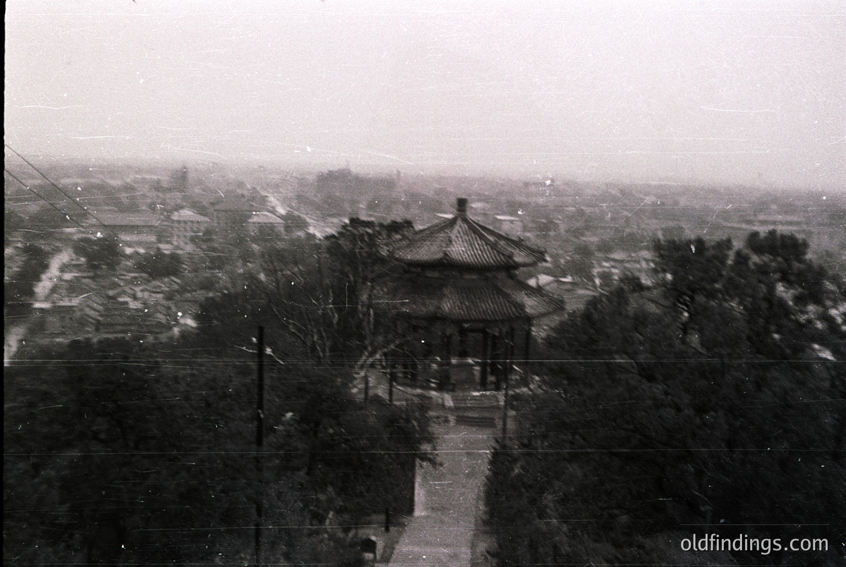 Vintage black-and-white photo of a traditional **Chinese pavilion** with upturned eaves, set atop a stone platform. Dense foliage surrounds the structure, with a distant urban landscape visible beyond. Likely **Qing Dynasty** (1644–1912) or early 20th-century architecture. Ideal for historical research or East Asian design references.