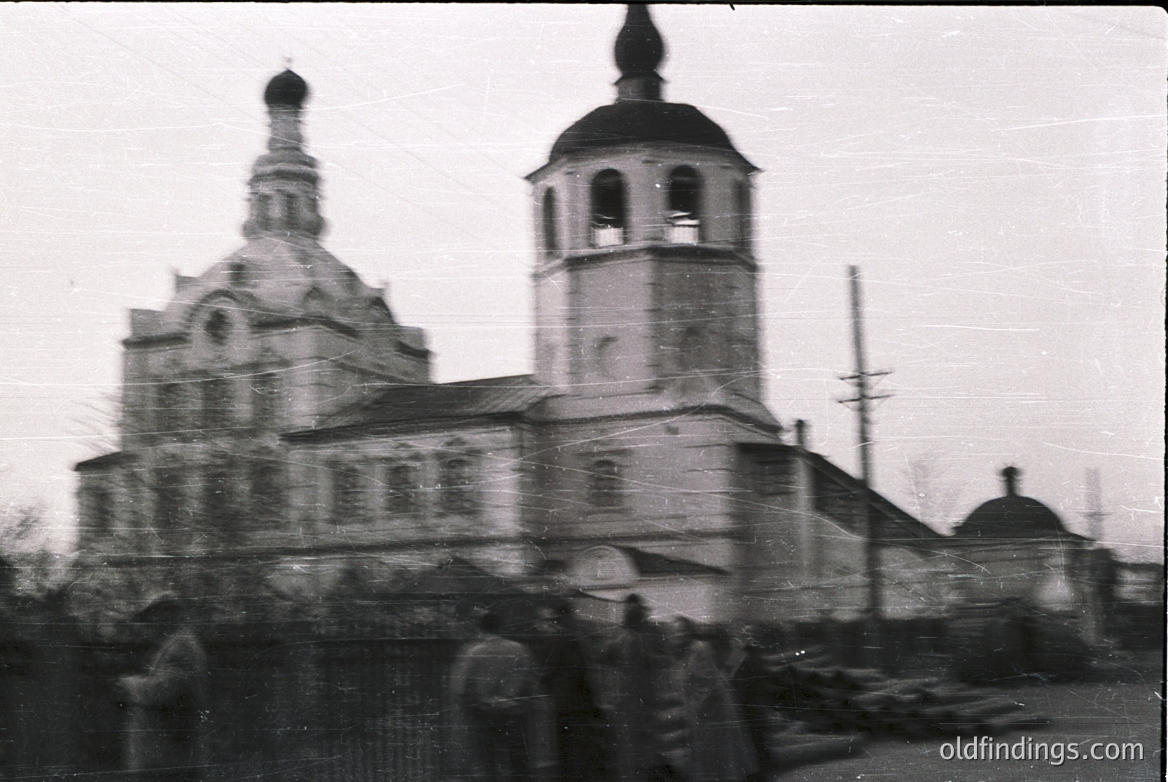 Russian Orthodox church with twin towers and onion domes, likely from the Soviet-era –1970s. Blurred crowd suggests outdoor gathering or procession. Architectural details include arched windows and brick construction. *(Note: Exact location indeterminate but stylistic cues align with Russian Orthodox design.)*