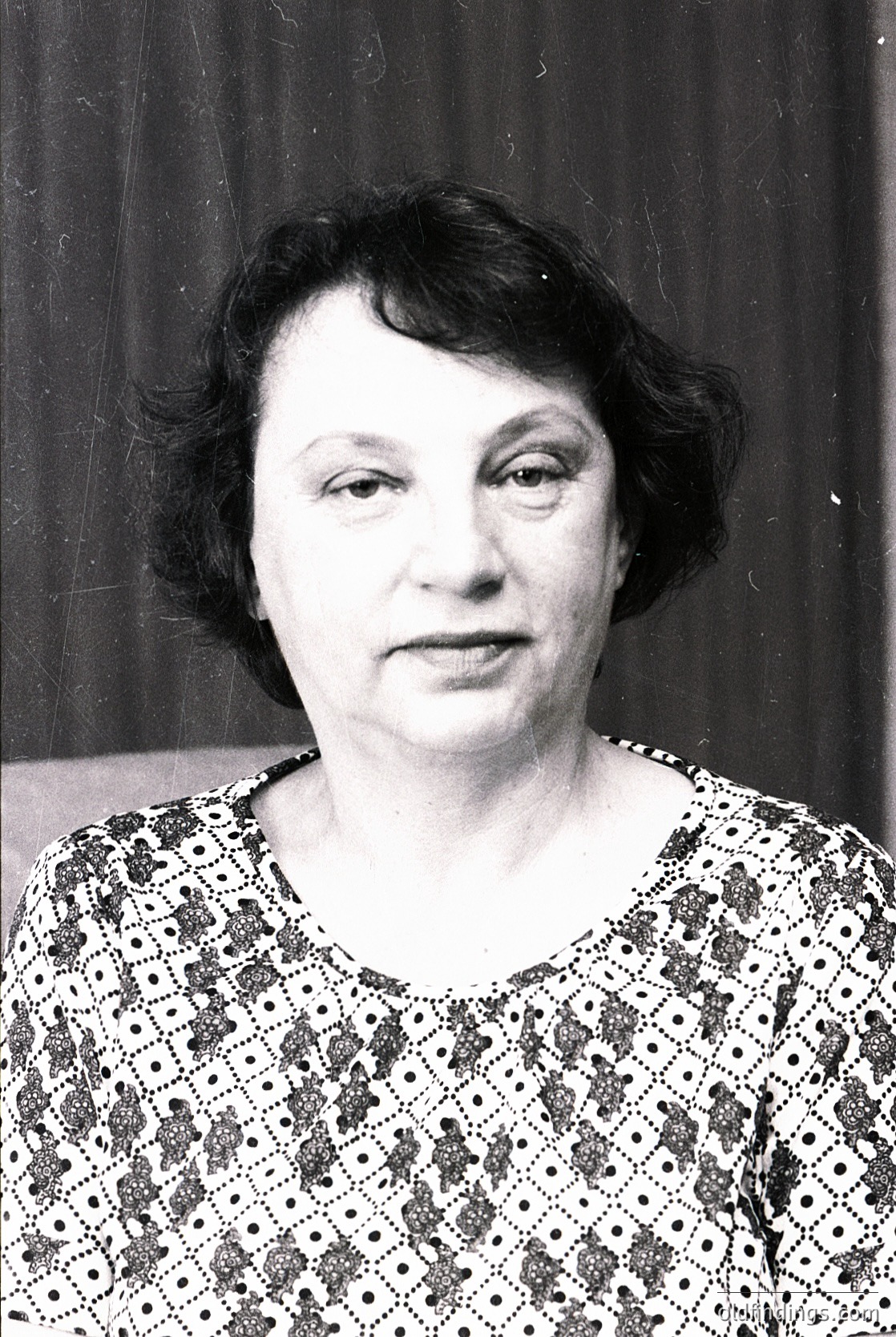 Portrait of an individual in a patterned blouse with geometric floral motifs, shot in black-and-white. Mid-century styling suggests or . Neutral backdrop hints at studio or formal setting.