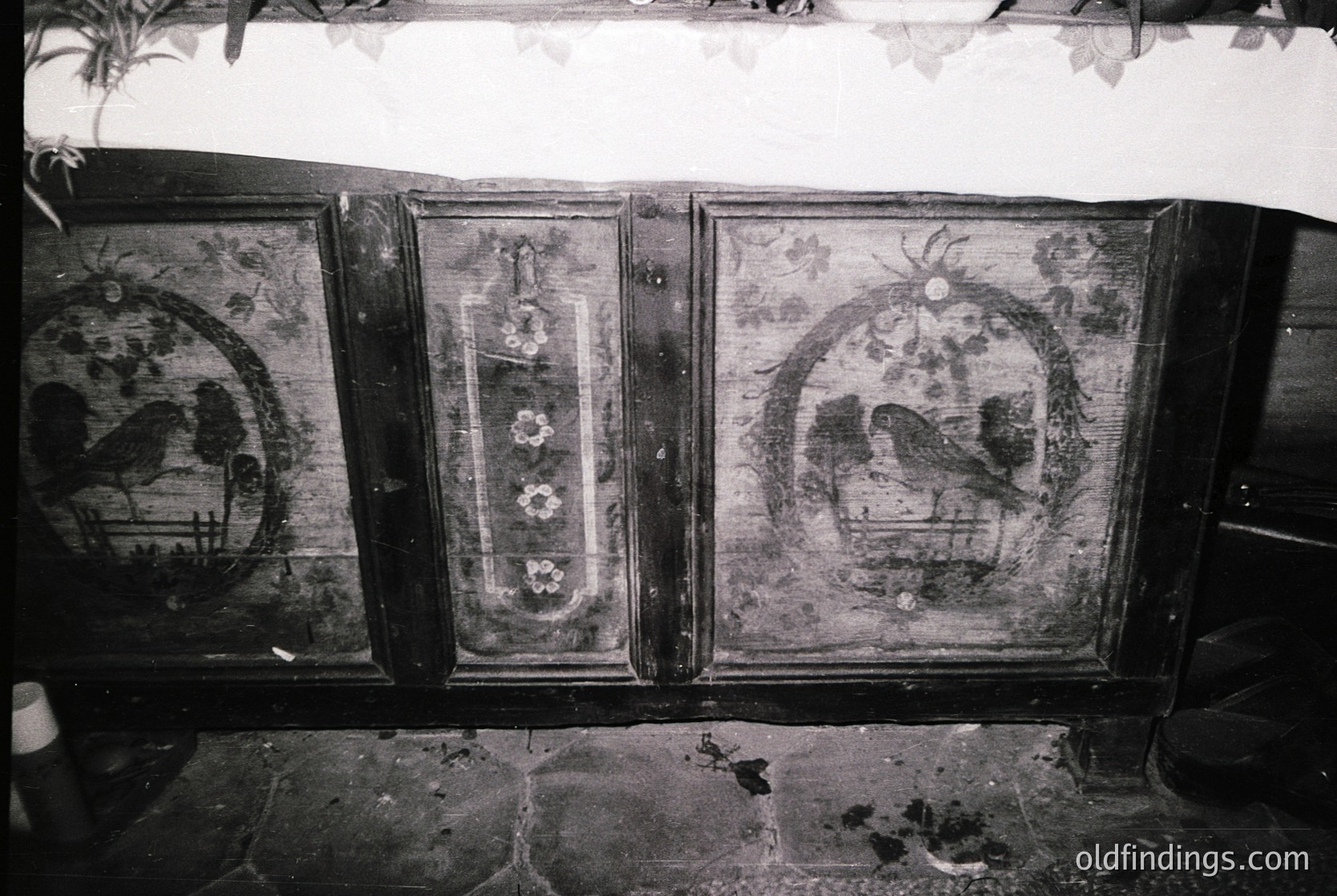 Vintage wooden cabinet with intricate folk-art painted panels, featuring symmetrical floral motifs and bird designs. Center panel displays faded floral wreath with floral clusters. Likely Eastern European, 19th–early 20th century.