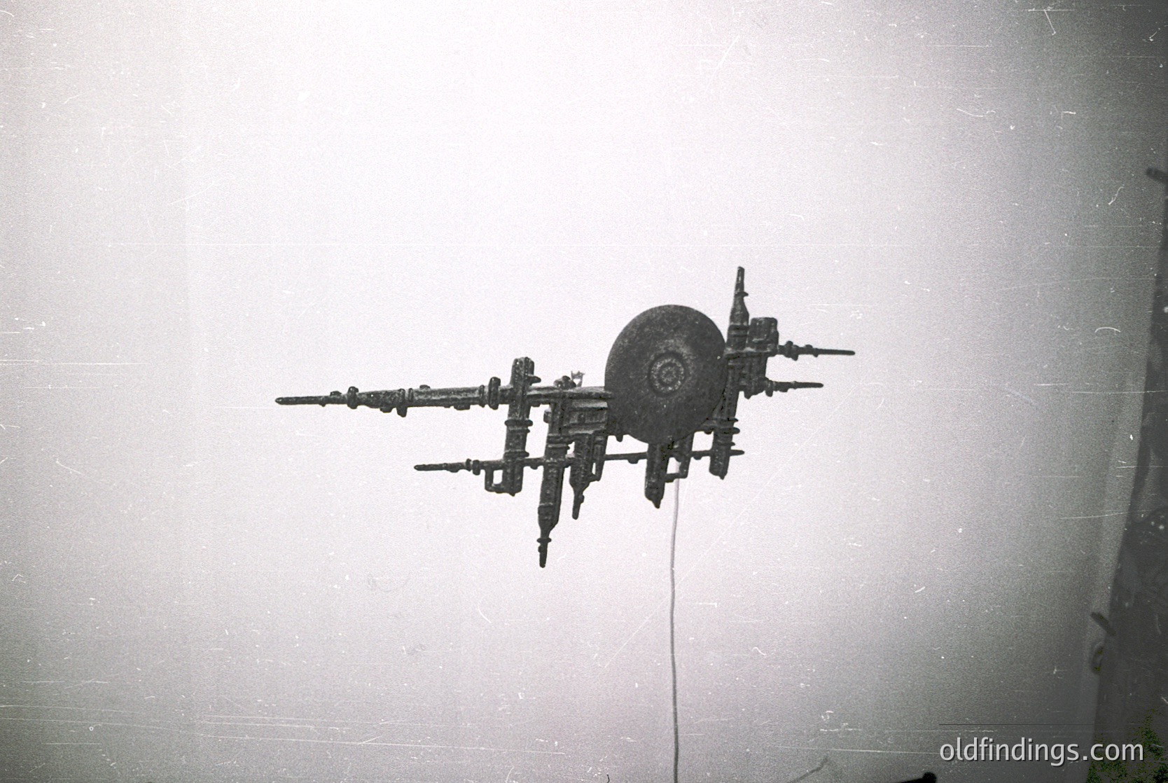 Vintage industrial silhouette of a mechanical arm with a circular wheel attachment, mounted on a plain wall. Likely a 20th-century factory or workshop setup.