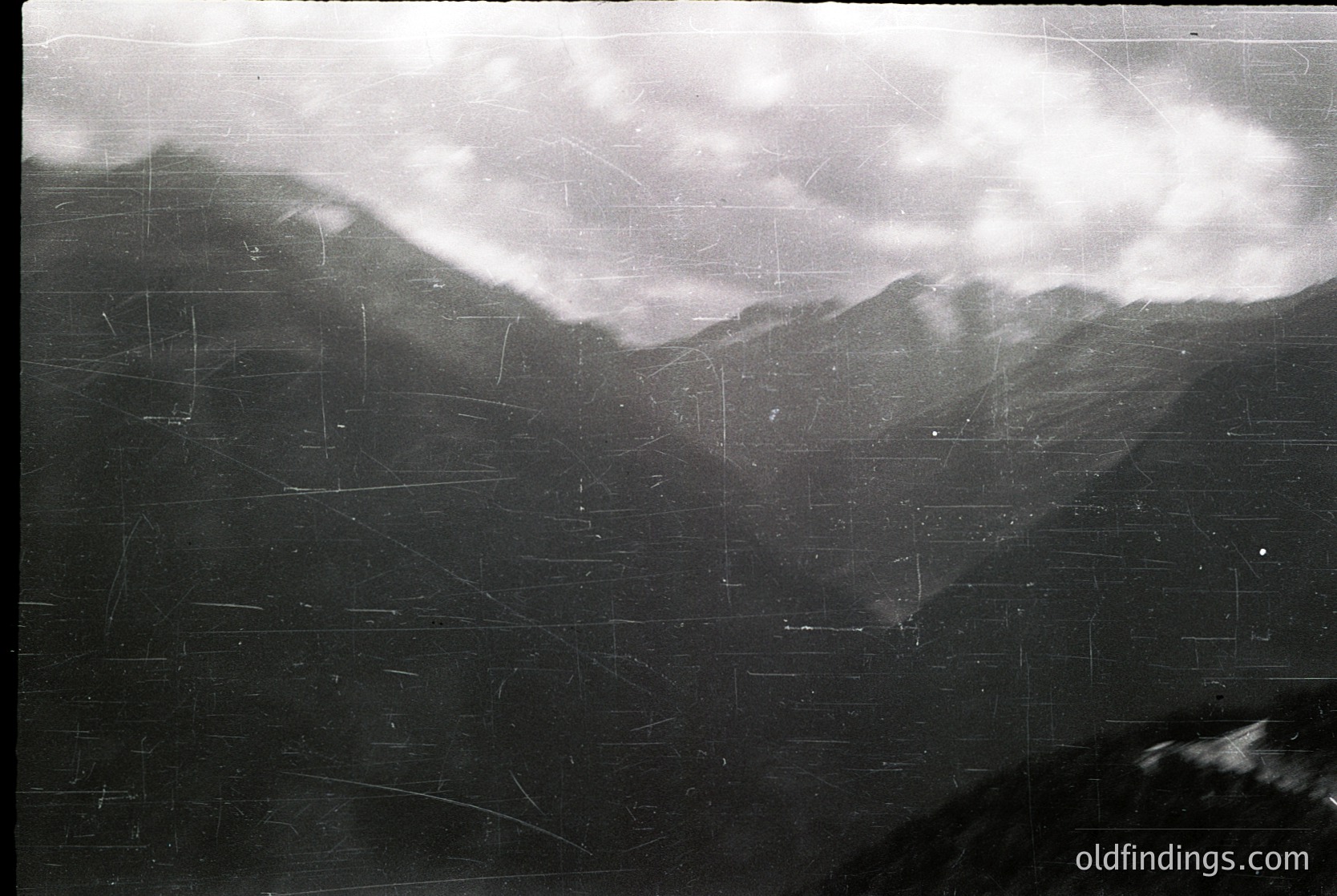 Vintage black-and-white aerial view of rugged alpine terrain with dense cloud cover. Visible grid lines suggest a topographic map overlay. Likely 20th-century military or cartographic survey. --- *Note: Grid lines and cloud cover suggest potential military or scientific use, but no specific location is identifiable.*