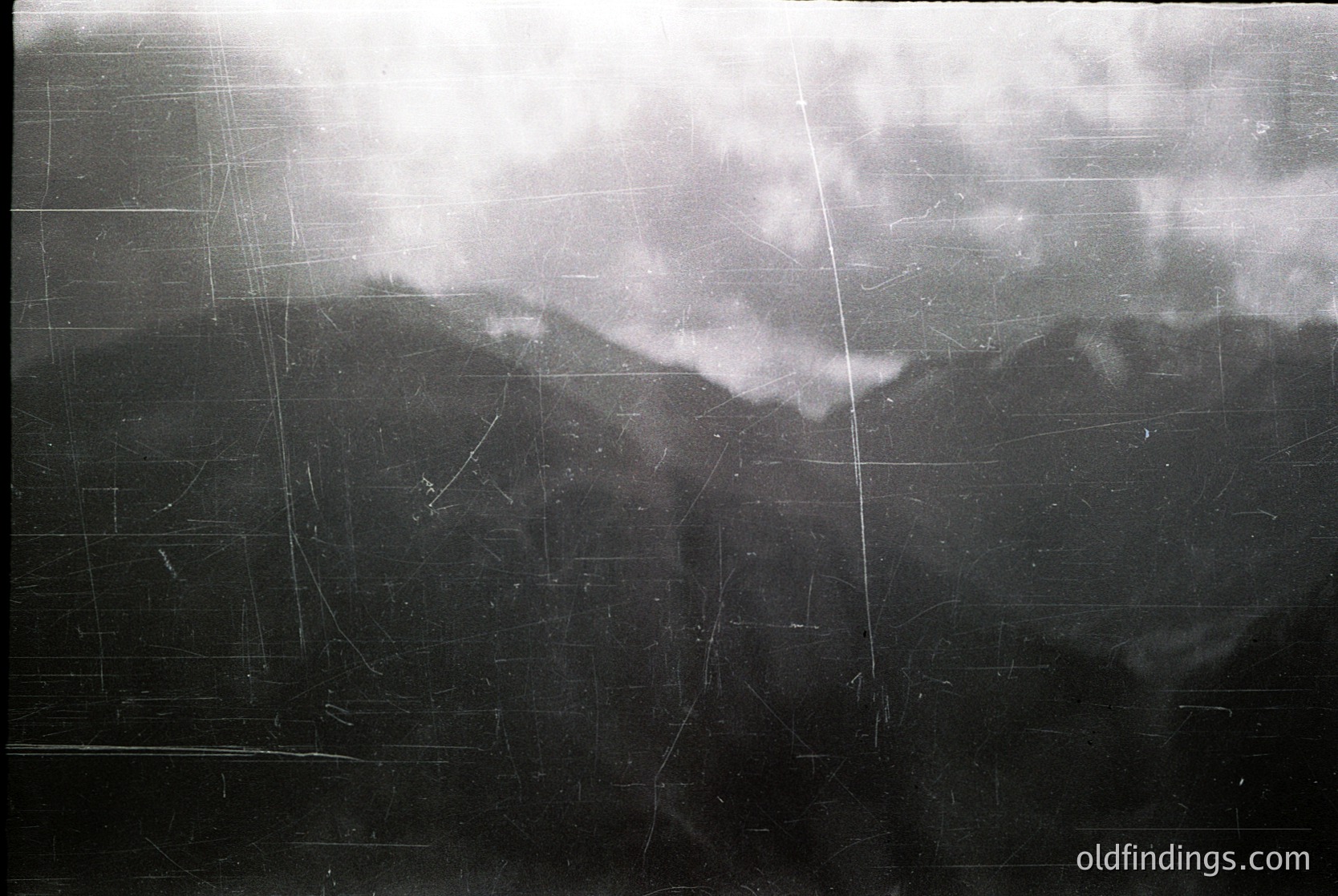 Vintage black-and-white aerial view of a grid-patterned agricultural field with faintly visible furrows, likely plowed for crop planting. The horizon shows distant, mist-shrouded hills under overcast skies. *(Note: Geographic location inferred as likely rural U.S. based on furrow patterns and style, but not definitive.)*