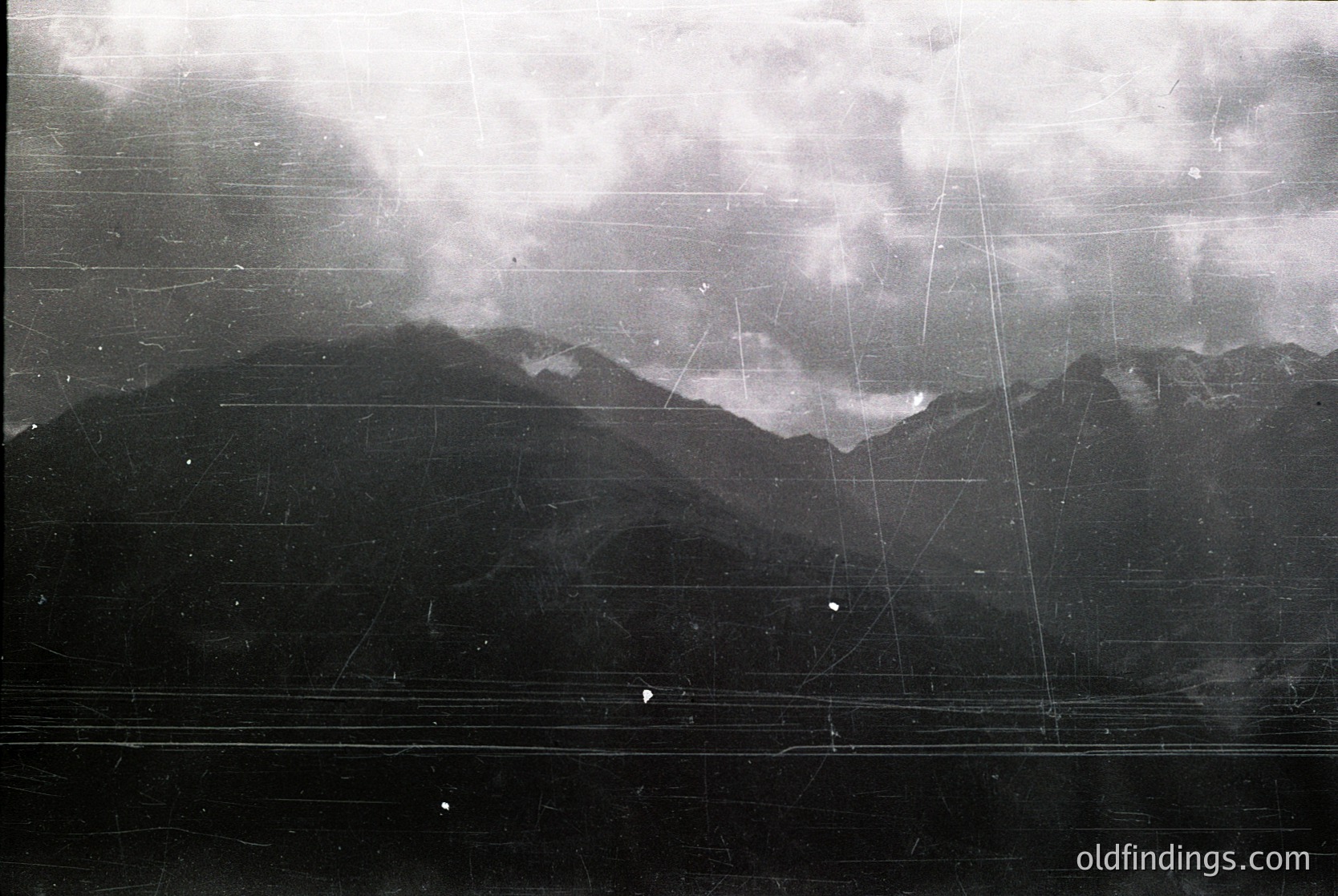 Aerial black-and-white photo of rugged mountain terrain with visible grid lines, likely from early 20th-century surveying or mapping. Distinctive jagged peaks and dense cloud cover suggest alpine or highland region.