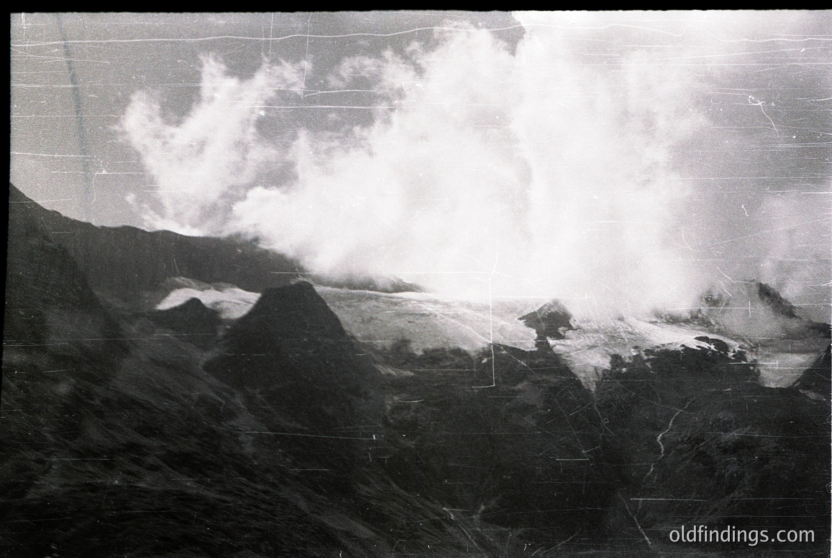Volcanic eruption plume billowing over rugged terrain, likely a stratovolcano. Dense ash cloud obscures distant slopes, suggesting active eruption. Vintage black-and-white print with visible grain, indicating mid-20th century photography.