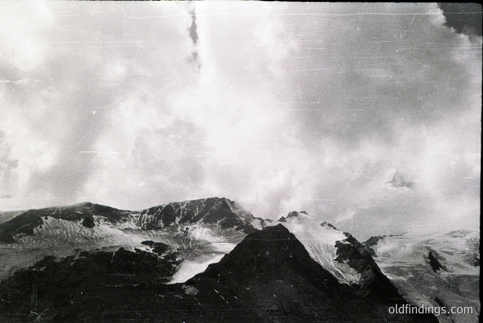 Vintage black-and-white aerial view of rugged volcanic terrain with jagged peaks and steep slopes. Dense cloud cover obscures upper elevations, emphasizing dramatic contrasts. Likely mid-20th century exploration or scientific documentation.
