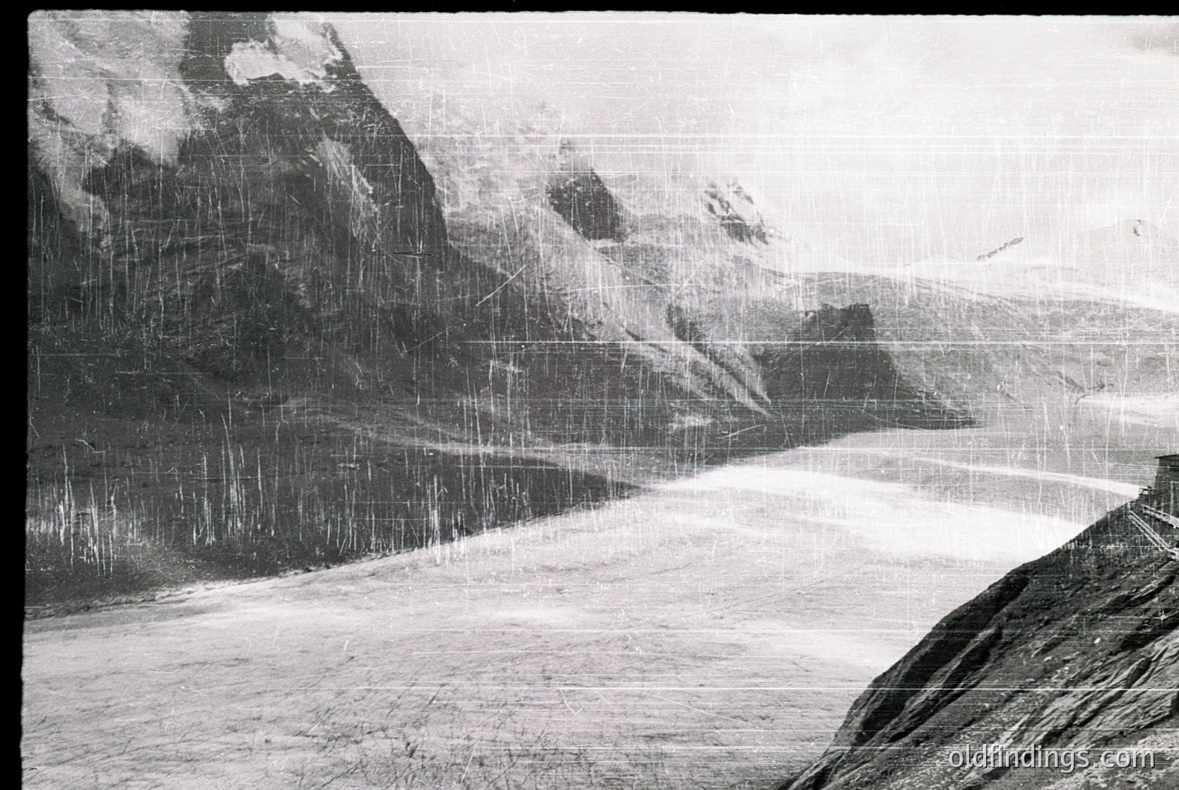 Vintage black-and-white alpine scene showing snow-laden pine forest and jagged peaks. Heavy snowfall obscures visibility, creating a dramatic, misty atmosphere. Likely early-to-mid 20th century, possibly for stock nature/landscape archives.