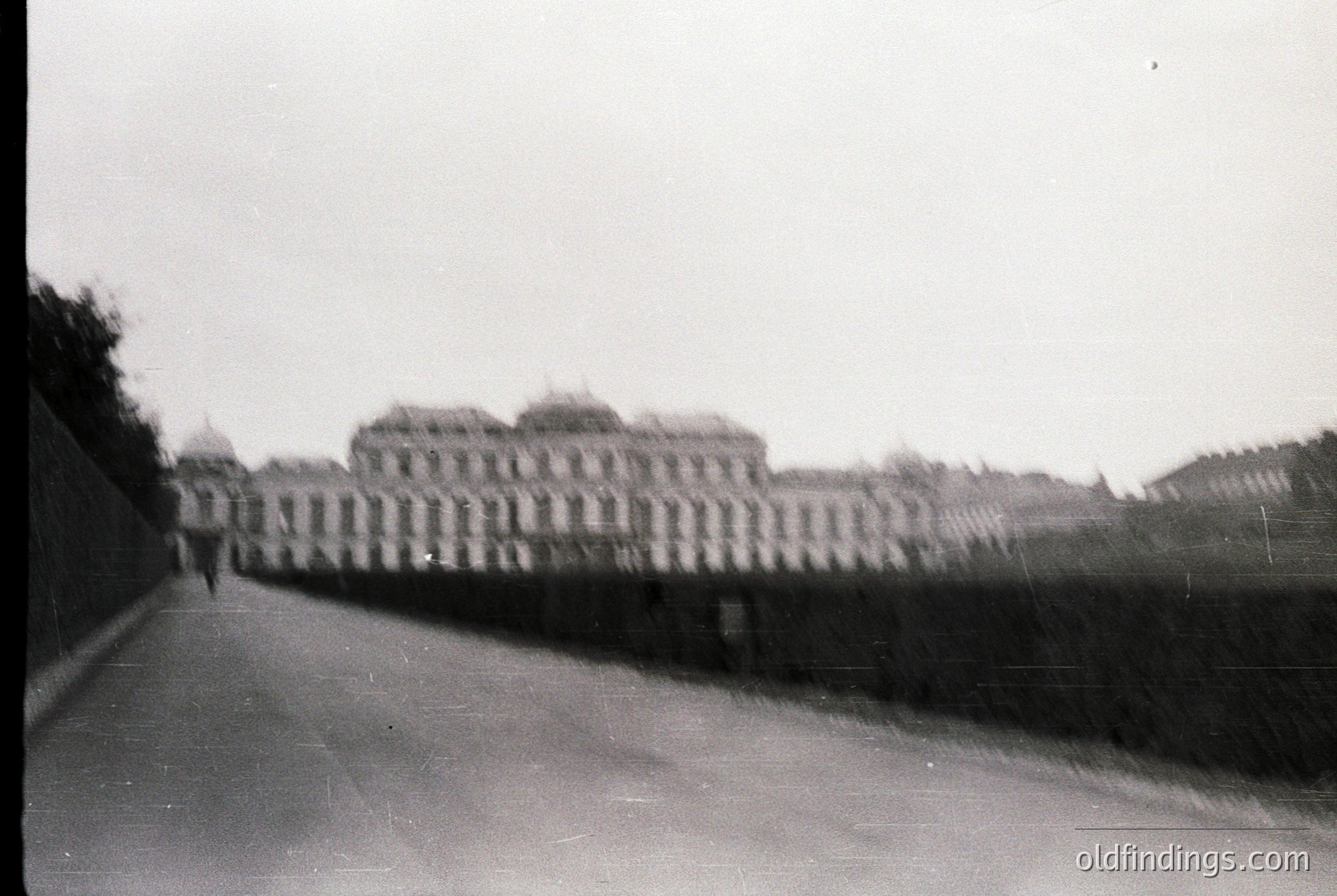 Blurred black-and-white shot of a grand, symmetrical palace façade with arched windows and a high wall, likely European. Overcast sky and indistinct pathway suggest early/mid-20th century architecture. Potential historical or stock use for vintage design references.