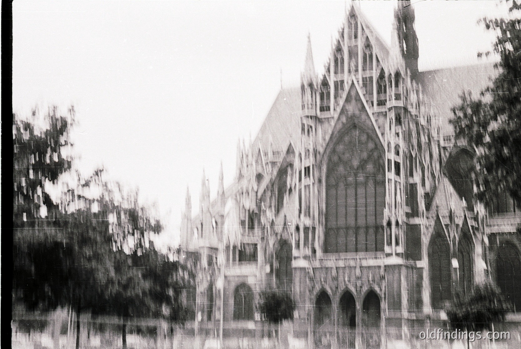 Gothic-style cathedral façade with pointed arches, stained-glass windows, and intricate stonework. Blurred foreground suggests motion or vintage film grain. Likely mid-20th century architectural photography.