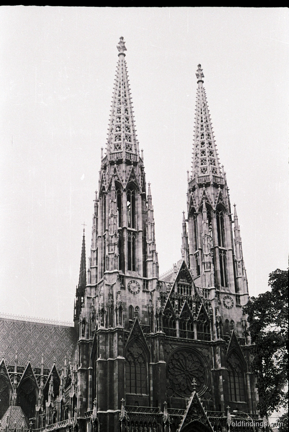 Gothic twin spires with intricate tracery and pointed arches, likely part of a 14th-century cathedral. The facade features a clock and ornate rose windows, characteristic of European Gothic architecture. Potential location: Vienna, Austria ().