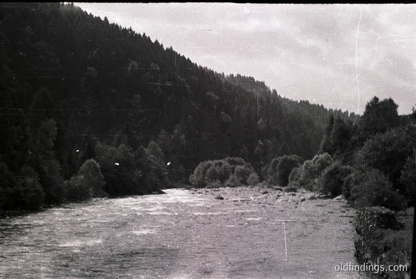 Black-and-white river scene with dense forest on both banks, flowing through a valley. Distinctive rocky outcrops and shallow rapids visible. Likely early-to-mid 20th century based on grain and toning.
