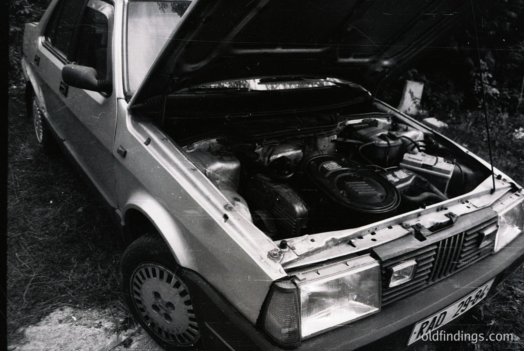 Classic **Volvo 740** with open hood showcasing inline-5 engine, likely **1980s** production. Rust and wear suggest vintage restoration or classic car scene. Front license plate visible.