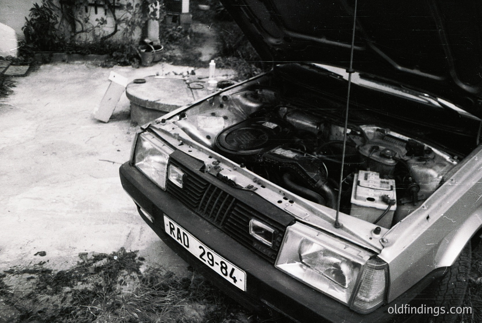 Vintage sedan with open hood revealing classic inline engine, likely a Škoda from the 1970s–80s. Rust and wear suggest long-term use in a garage setting. License plate "RD 29-84" indicates Eastern Bloc registration. Industrial, nostalgic, and utilitarian aesthetic.