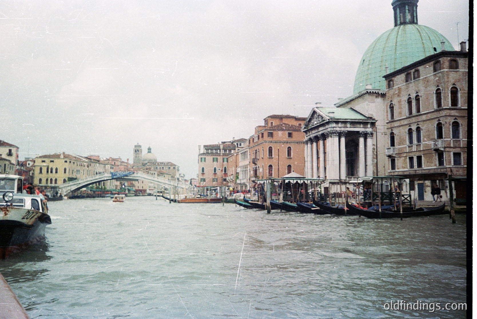 Venetian canal scene with historic architecture: domed church, arched bridges, and moored gondolas. Overcast sky enhances atmospheric depth. Likely late 20th century,