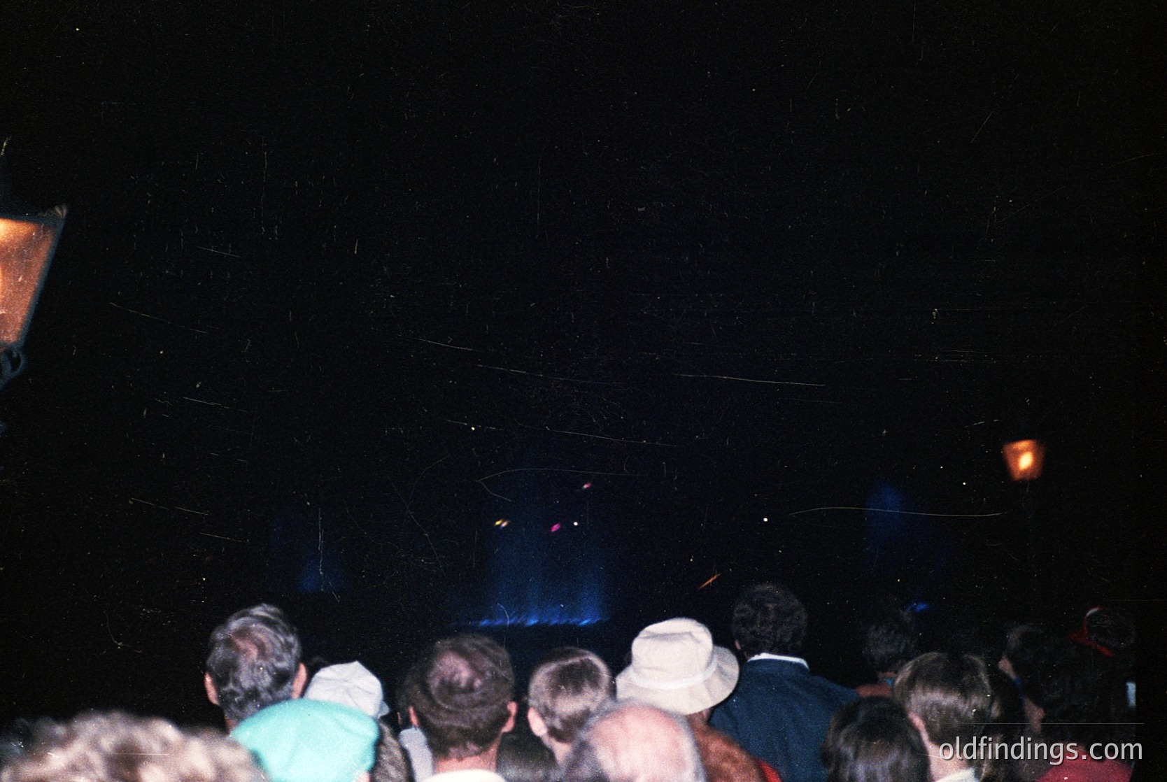 Vintage concert crowd shot, low-light stage lighting reveals blue haze. Casual 1990s attire—hoodies, caps, and jeans—suggests indie/rock venue. Crowd faces stage, silhouetted against dark backdrop. Potential or reference.