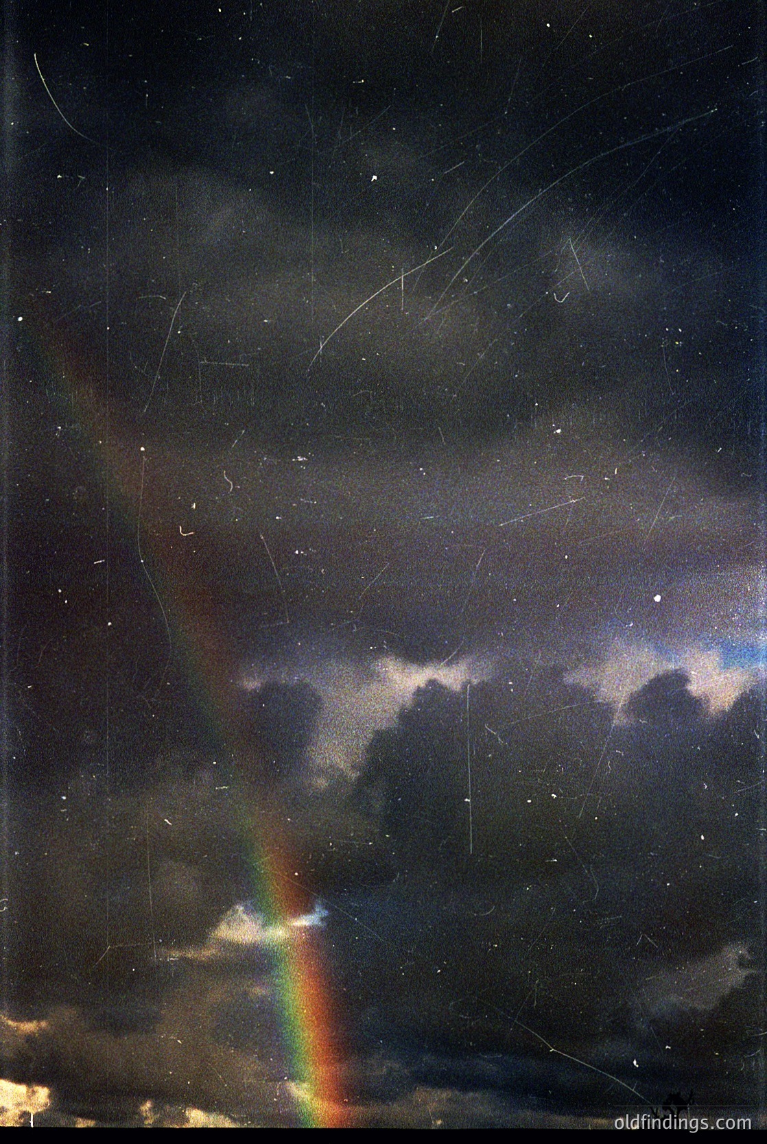 Vintage wet-plate or early film capture of a dramatic nighttime rainbow over storm clouds, with visible scratches and grain. Likely 19th-century photography due to texture and lighting.