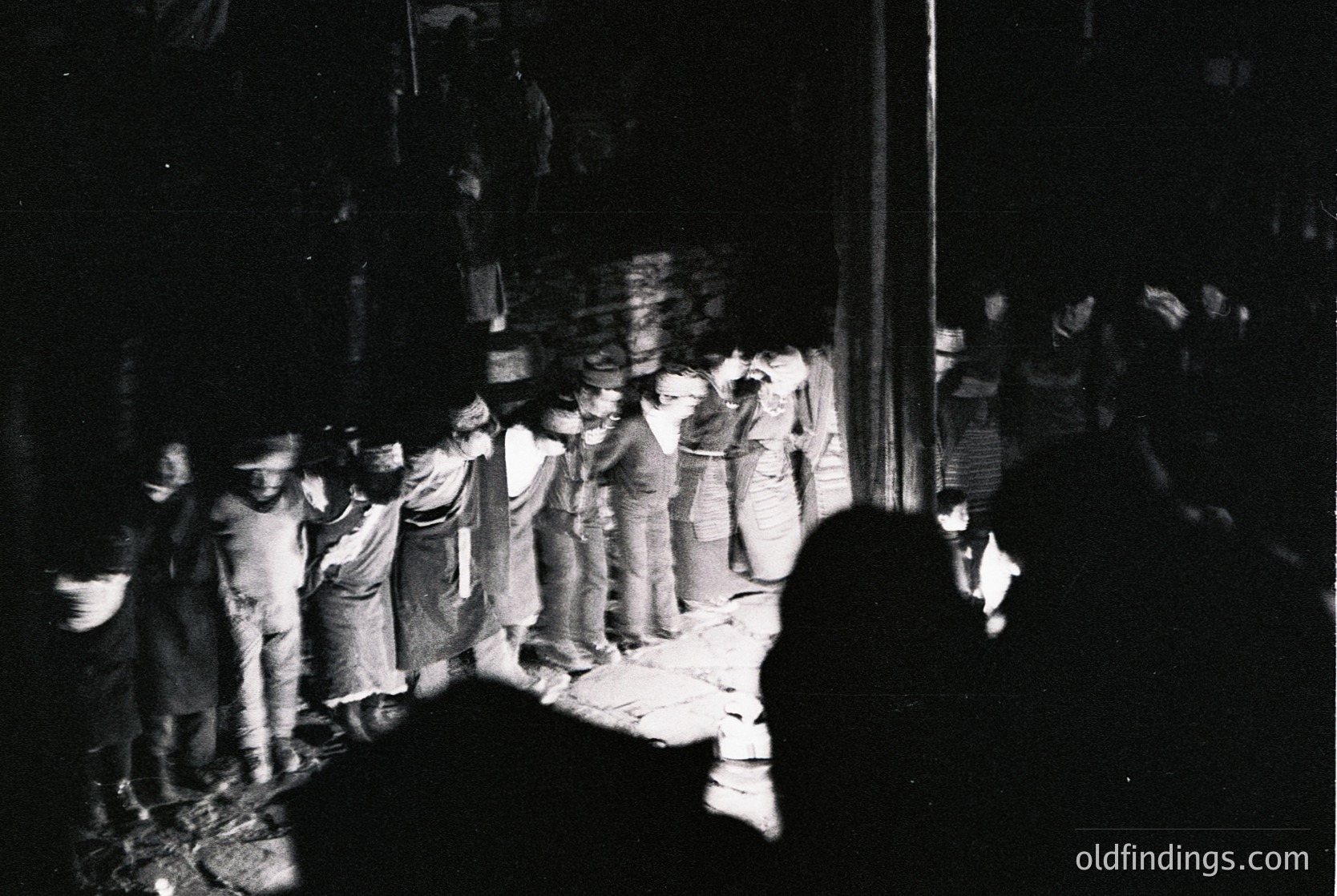 Crowd of men in 1960s-era suits and hats gathered outdoors at night, likely during a public event or demonstration. Motion blur suggests movement or rapid shutter speed. Urban setting with indistinct architecture in background.