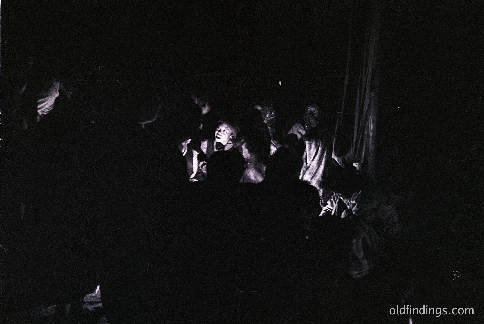 Vintage black-and-white photo of a crowded, dimly lit indoor gathering with silhouetted figures dancing. Dynamic poses suggest energetic movement, likely a social event or party. Undefined location but evokes mid-20th century nightlife culture.