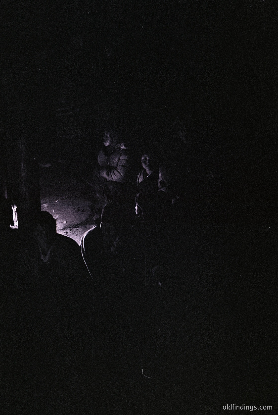 Low-light portrait of a person with blurred facial features, illuminated by a single overhead light source. The silhouette reveals a hairstyle with layered, wavy texture. Style suggests mid-20th century fashion, possibly 1950s–1960s. Ideal for moody, atmospheric stock photography or historical research.