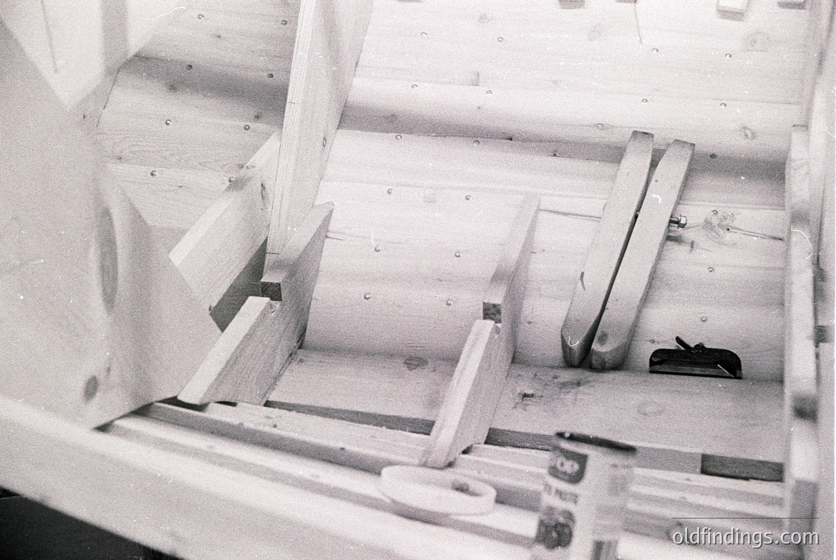 Industrial woodworking machinery with angled, precision-cut wooden planks in a clamping station. Likely a 20th-century sawmill or furniture factory setup. Noticeable rivets and metal framework for stability.
