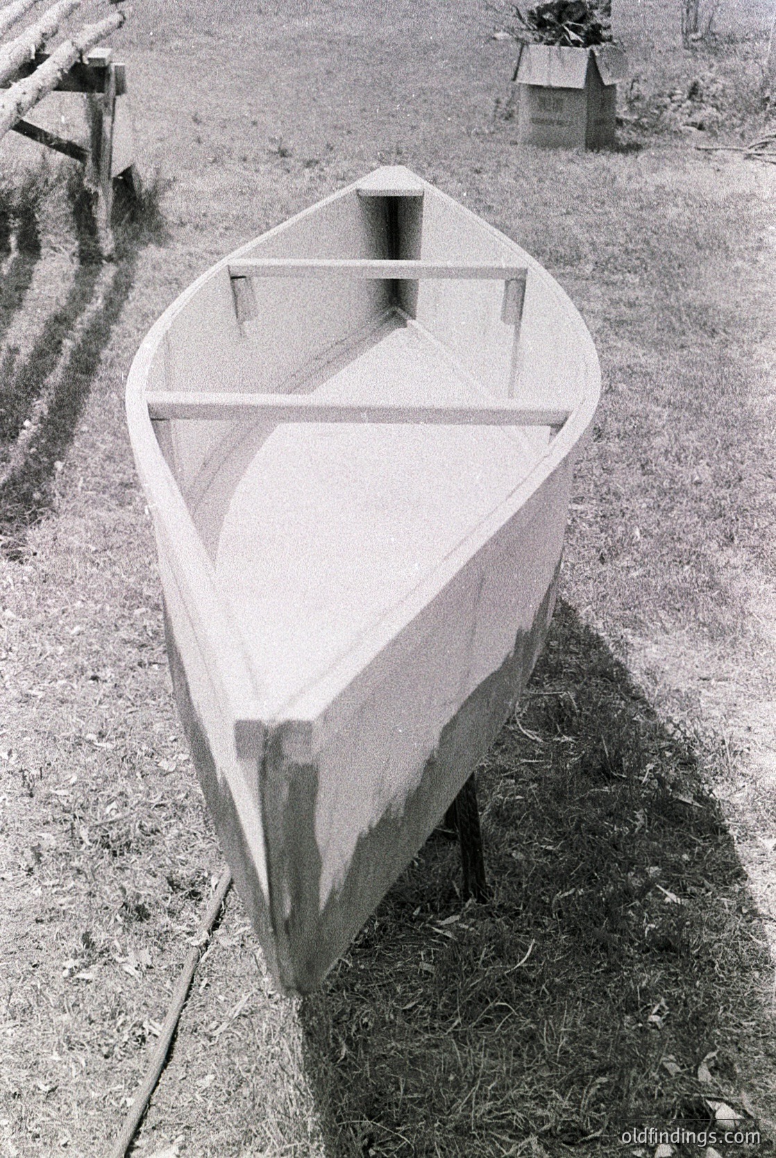 Classic wooden rowboat with simple crossbeam seating, resting on dry grass near a rural path. Likely mid-20th century design, emphasizing functionality over ornamentation. Ideal for vintage-inspired projects or historical research on small watercraft.