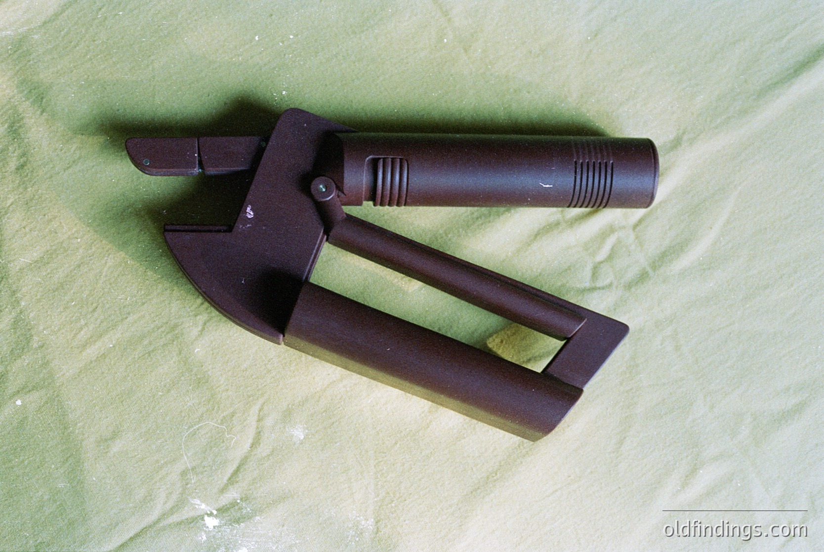 Vintage-style bolt cutter with dark brown, textured grip and forged metal jaws, resting on green fabric. Classic design for heavy-duty applications, likely mid-20th century industrial or automotive use.