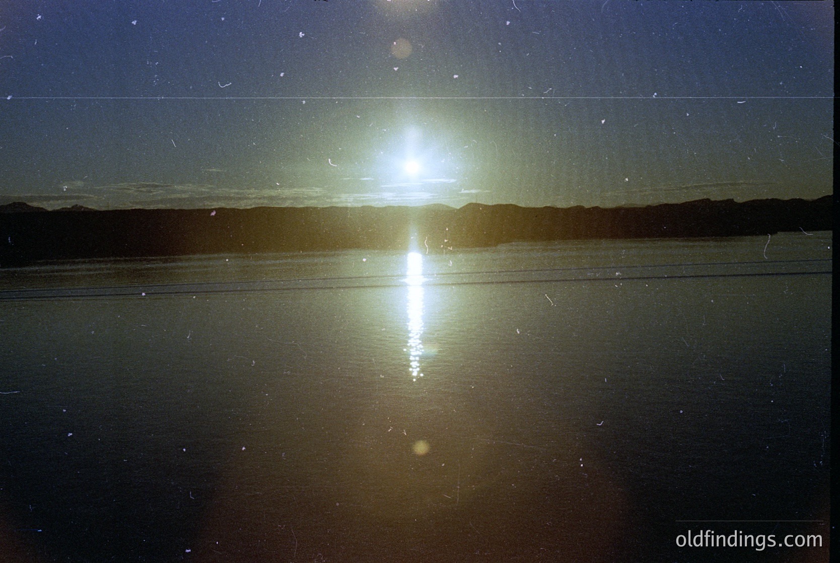 Sunburst reflection on calm water, likely a lake or coastal inlet, with lens flare creating symmetrical light patterns. Horizon shows faint silhouettes of distant land or mist. Ideal for nature, travel, and atmospheric photography.