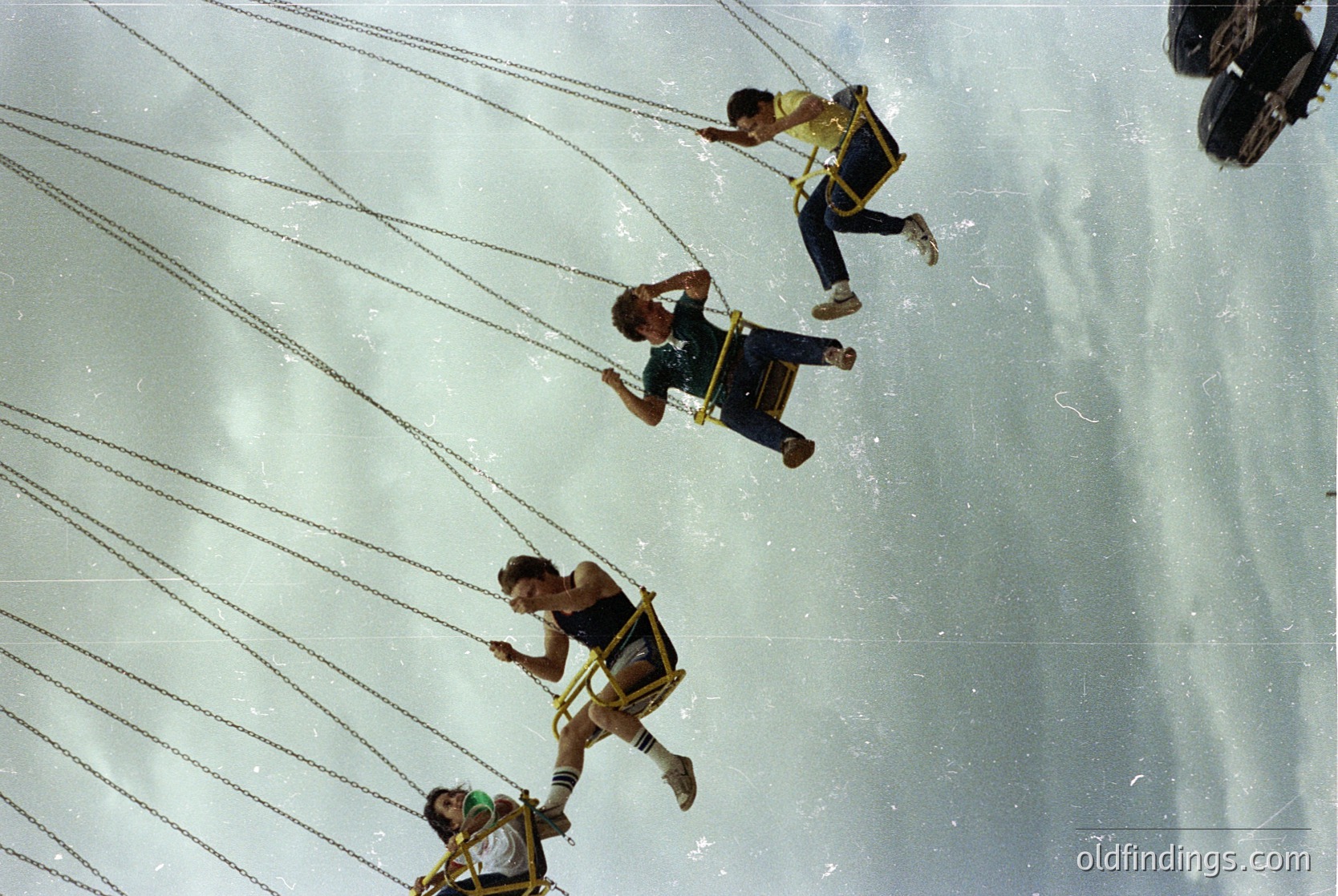 Aerial shot of four bungee jumpers mid-descent, harnessed and suspended by elastic cords. Bright yellow shorts and black harnesses contrast against the sky. Likely taken at a commercial bungee jump site.