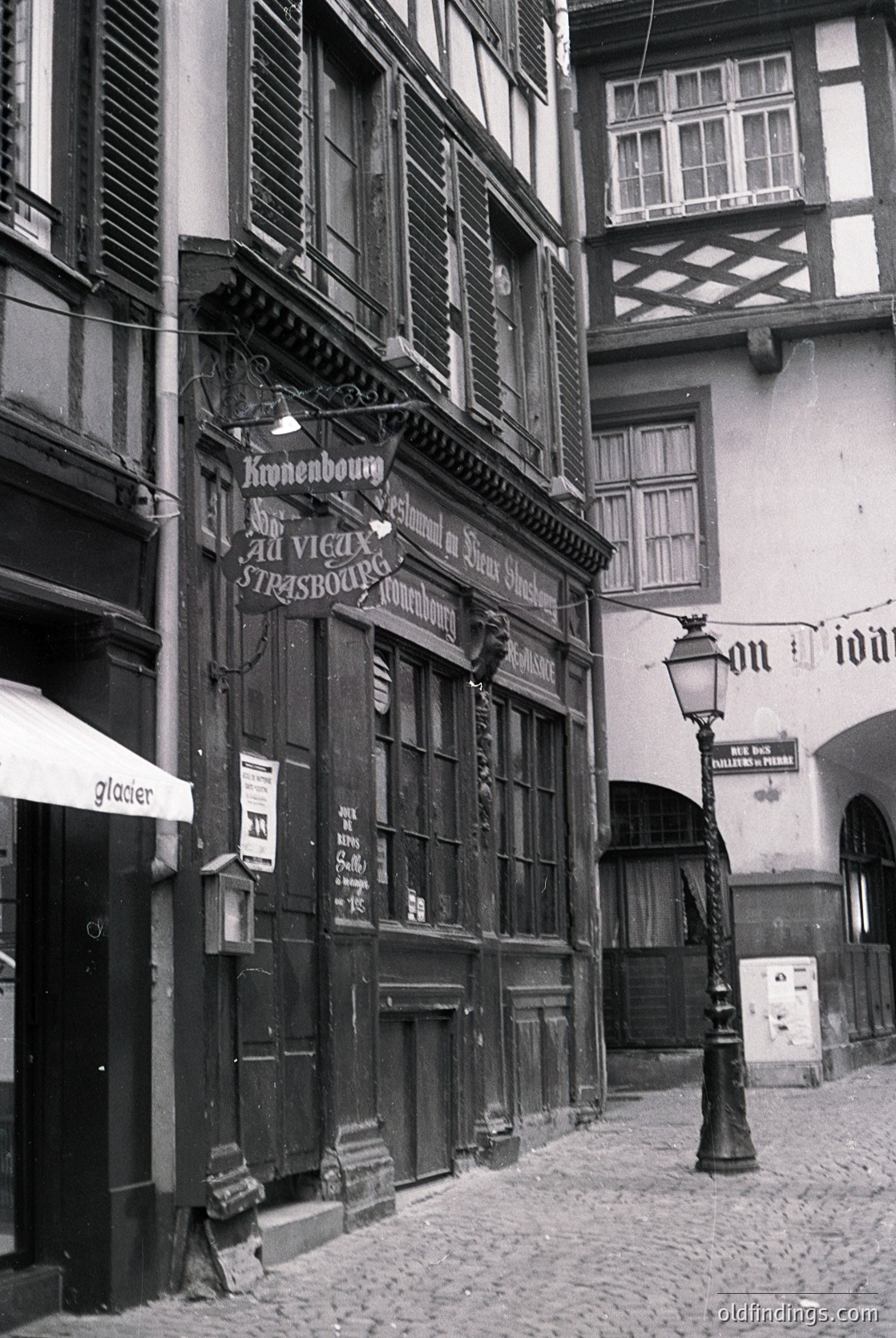 Historic Strasbourg timber-framed building with "Kronenbourg" beer signage, cobblestone street, and vintage street lamp.