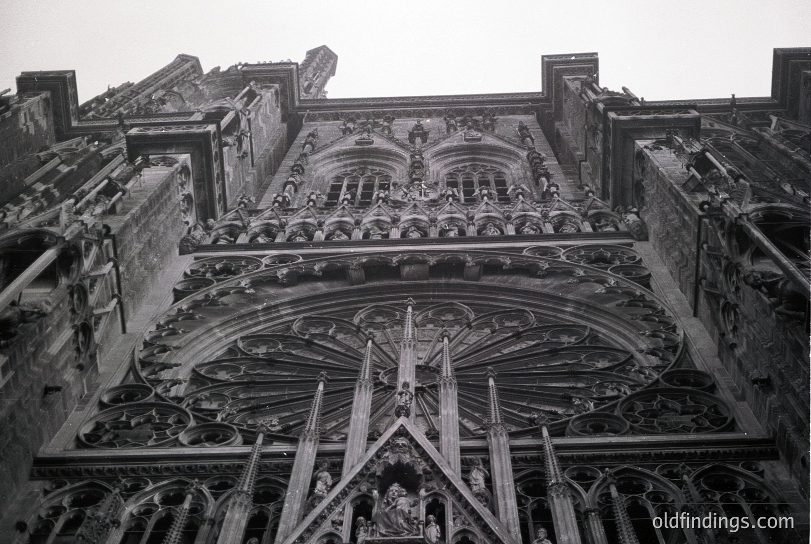 Gothic cathedral façade featuring intricate stone tracery, pointed arches, and sculpted figures. Likely 13th–16th century European architecture. Symmetrical rose window and elaborate reliefs dominate the central portal.