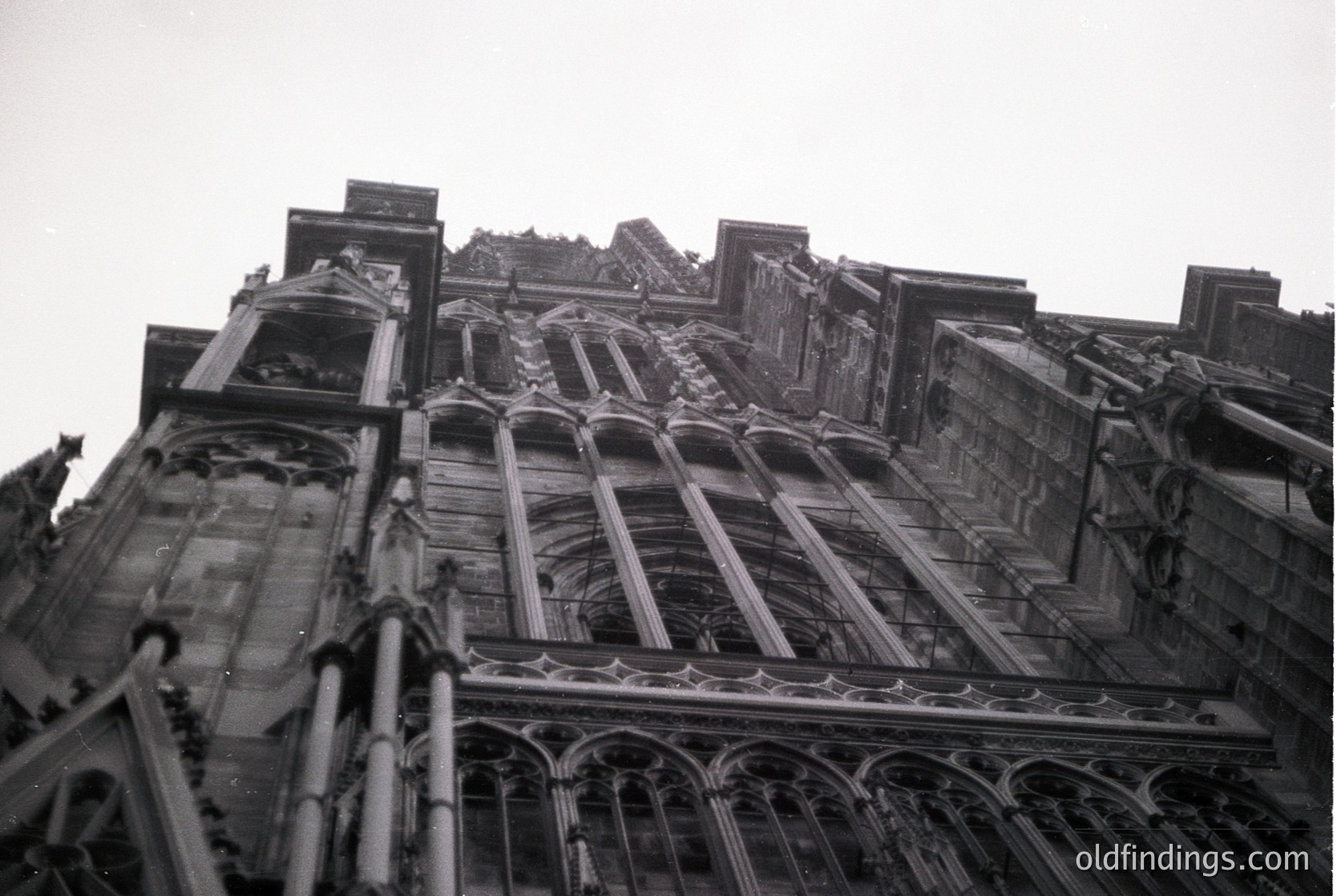 Gothic stone façade featuring pointed arches, intricate tracery, and buttresses—likely a European cathedral or church. Vertical perspective highlights vertical lines and decorative stonework. Mid-20th century black-and-white print.