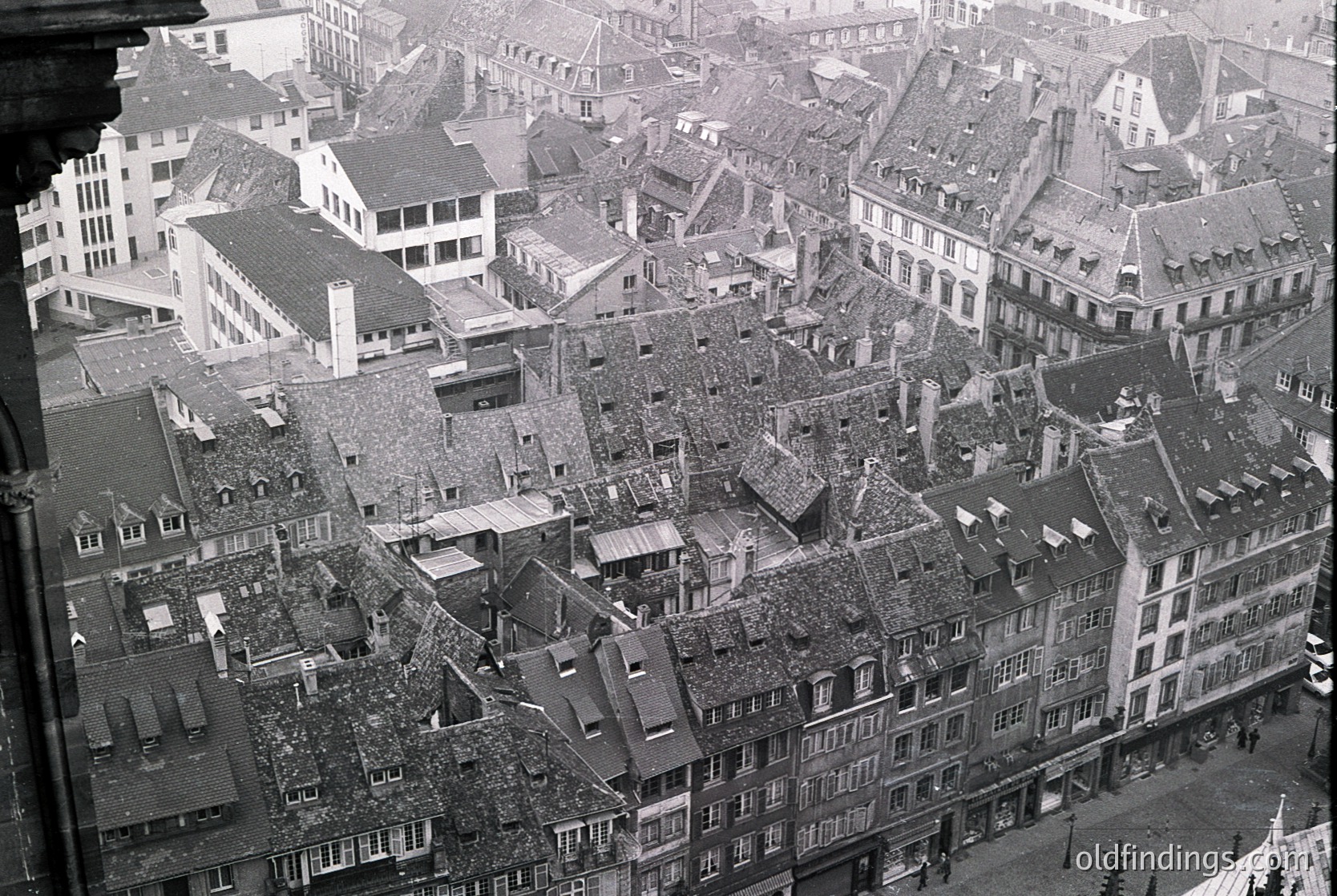 Dense urban rooftops and chimneys in a European city, likely post-WWII, showing bomb damage and reconstruction. Sloped slate roofs, gabled facades, and exposed debris dominate the scene. Architectural style suggests 19th-century origins with mid-century damage.