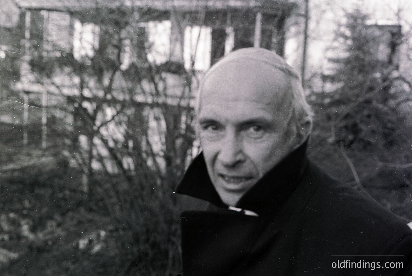 Black-and-white portrait of an elderly man in a clerical collar, likely a priest, outdoors with blurred winter trees in background. Mid-20th century attire suggests or . Expression conveys solemnity.