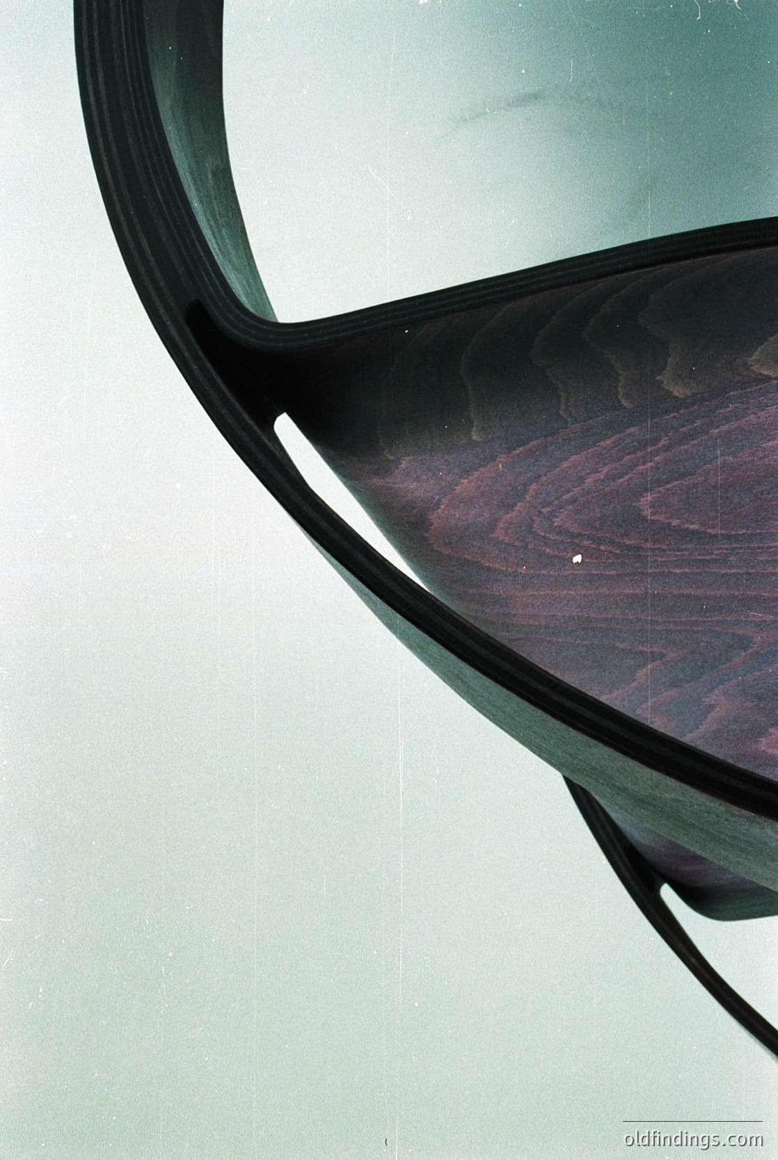 Mid-century modern chair with curved wooden seat and black metal frame, showcasing organic design. Reflective surface captures subtle light patterns. Ideal for interior design inspiration or vintage furniture research.