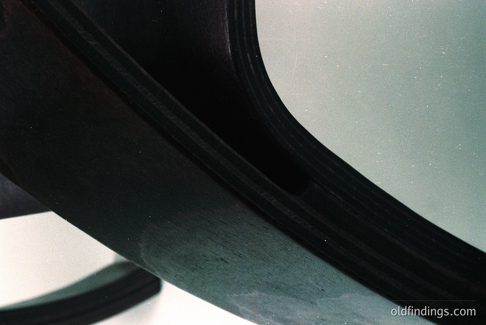 Close-up of a vintage car’s curved chrome fender, showing wear and minor scratches. Reflects muted indoor lighting, suggesting a garage or showroom setting. Likely mid-20th century automotive design (, , , , ).