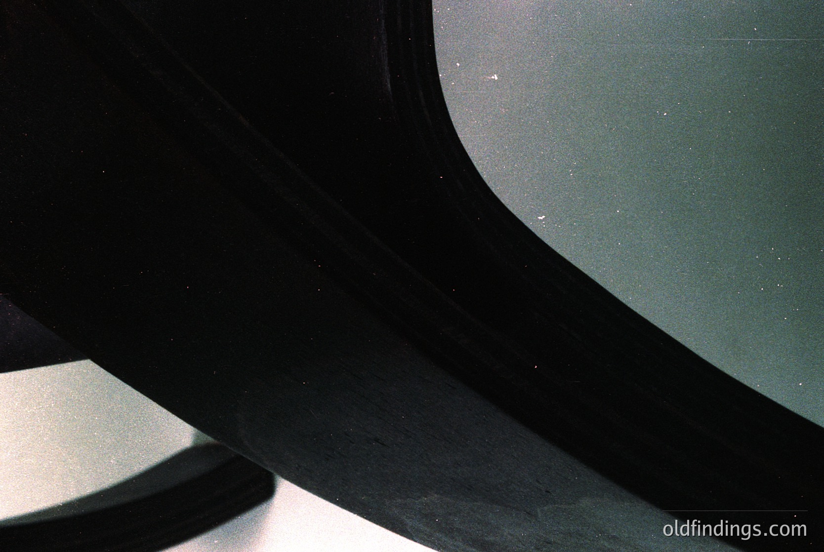 Close-up of a vintage car’s curved windshield and side mirror, showing subtle scratches and minor water spots. Reflects muted surroundings, likely an indoor garage or workshop. Style suggests mid-20th century automotive design (, , , , ).