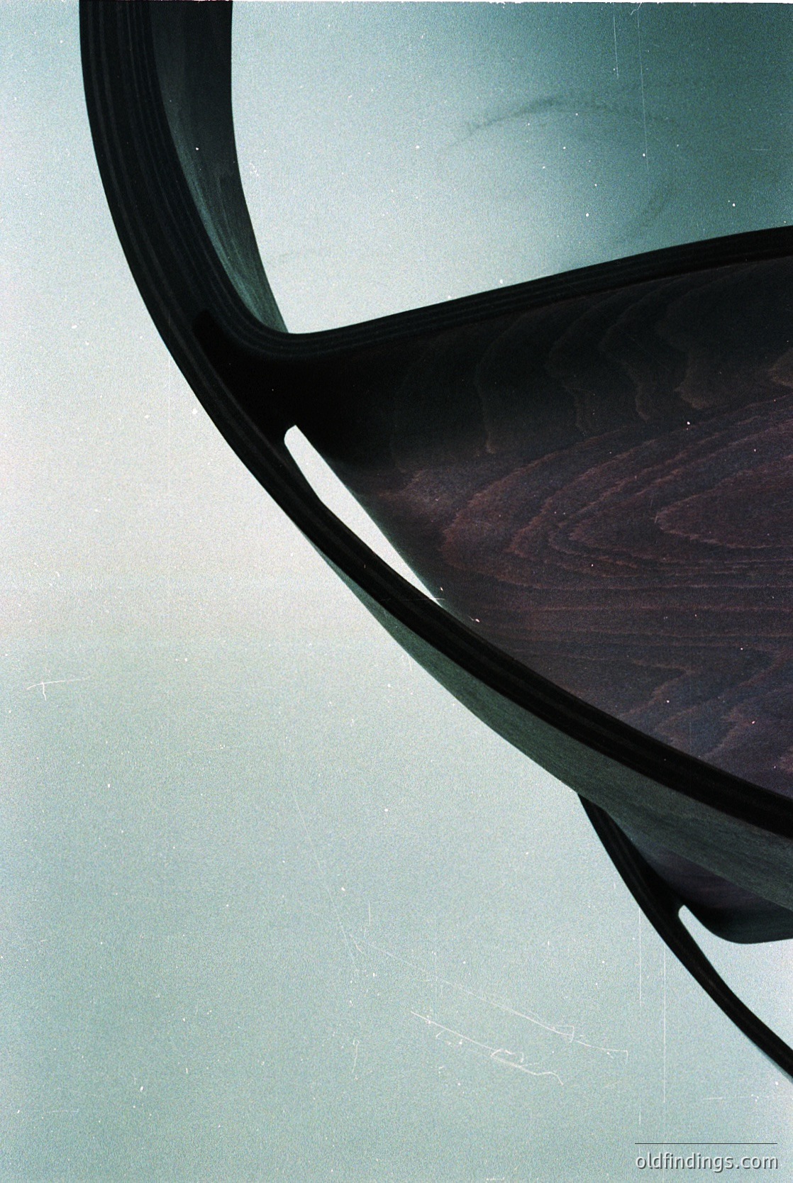 Mid-century modern chair with curved wooden seat and chrome/metal frame, showcasing organic design. Reflective surface captures subtle background distortion. Ideal for vintage interior or design reference.