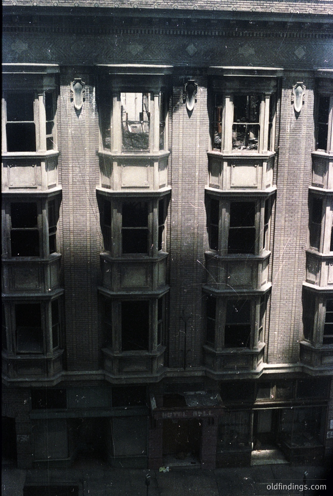Symmetrical brick facade featuring three bay windows with ornate stone detailing—likely Art Deco or early Modernist. Dark, arched window frames contrast with light brickwork. Reflective glass suggests urban residential or commercial use. Possible European setting, mid-20th century.