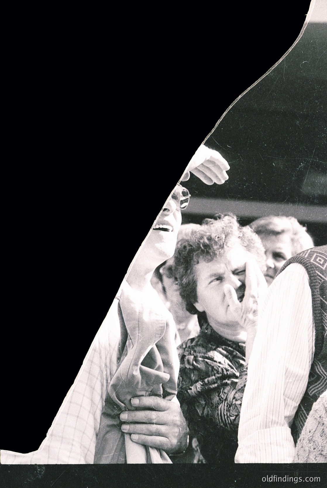 Black-and-white candid of elderly woman in patterned sweater adjusting her hair, framed by a dark car’s rearview mirror. Mid-20th century street scene, likely 1960s–1970s. Urban setting with blurred background suggesting motion.