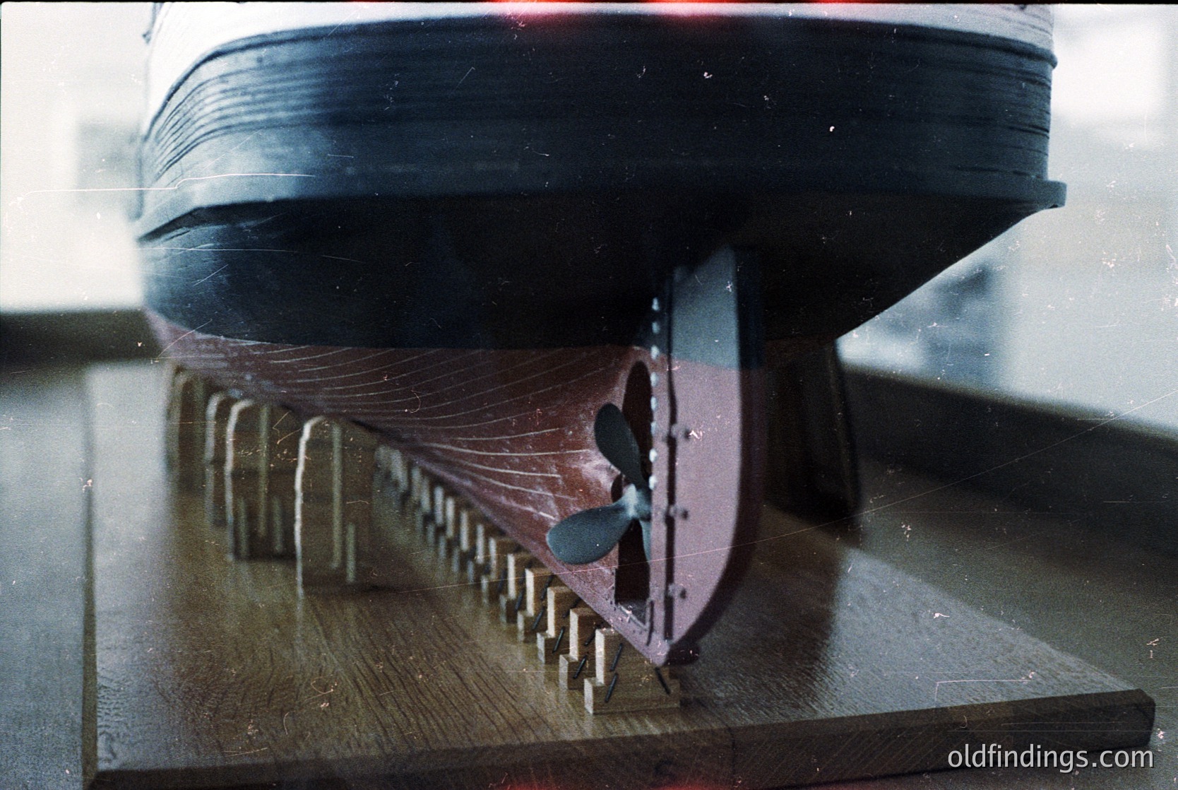 Close-up of a vintage ship propeller mounted on a wooden display stand, showcasing intricate blade details and rivets. Likely from a mid-20th-century maritime vessel.
