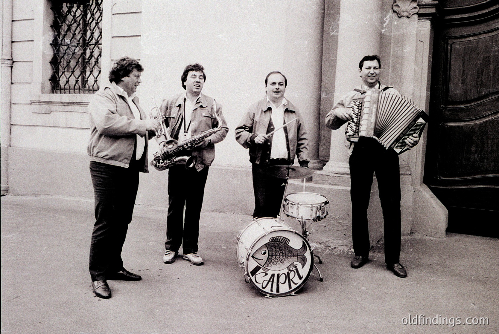 Street jazz quartet in 1970s Eastern Bloc attire—saxophonist, accordionist, drummer (with "APRIL" drum logo), and bassist. Urban setting with classical architecture. Likely Bulgaria or similar socialist-era city.