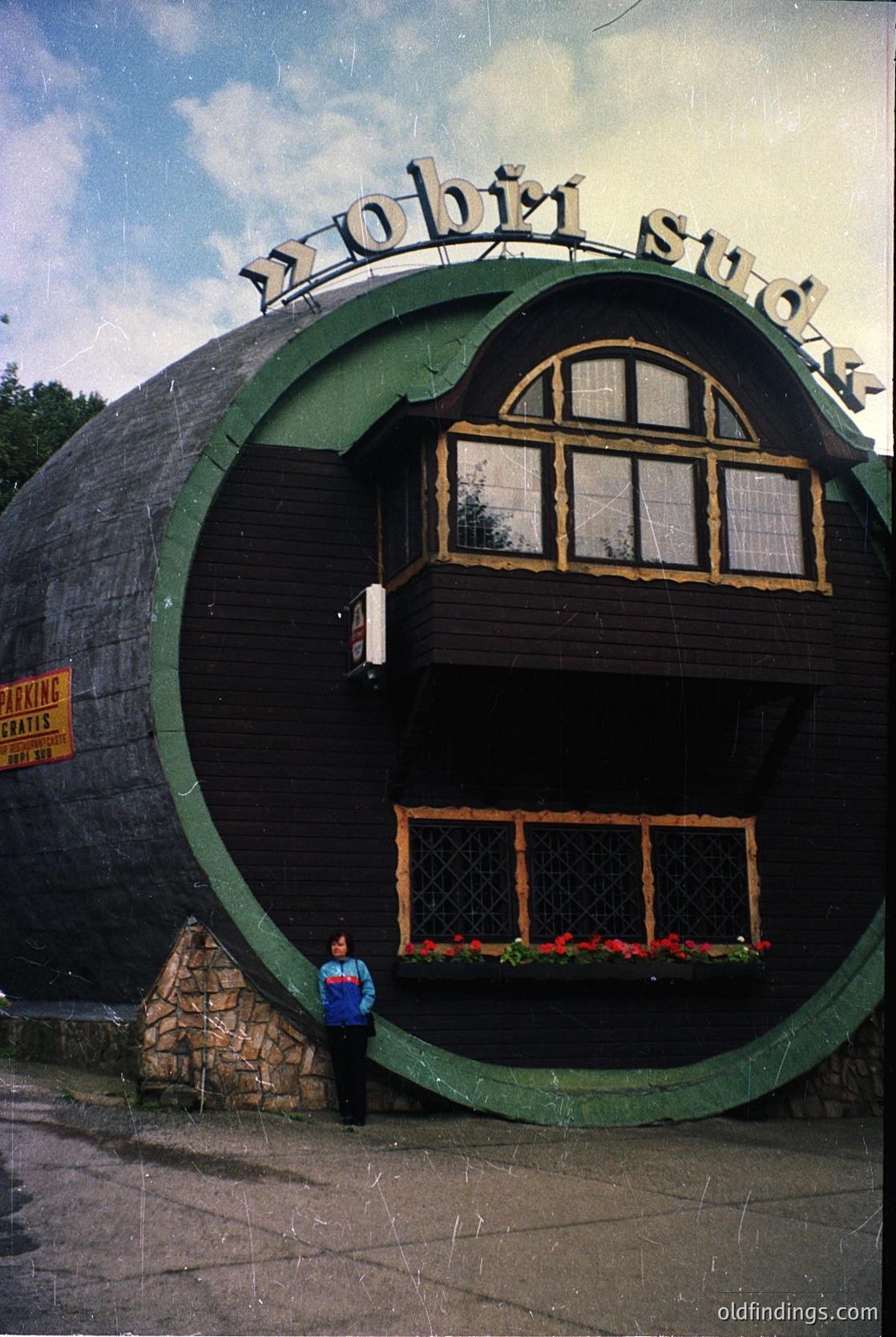 Vintage Soviet-era "Robič" soda factory repurposed as a café, featuring a distinctive circular brick facade with arched windows. The signage in Cyrillic suggests Eastern European location, likely Bulgaria. Mid-20th century industrial architecture with floral accents. éDesign