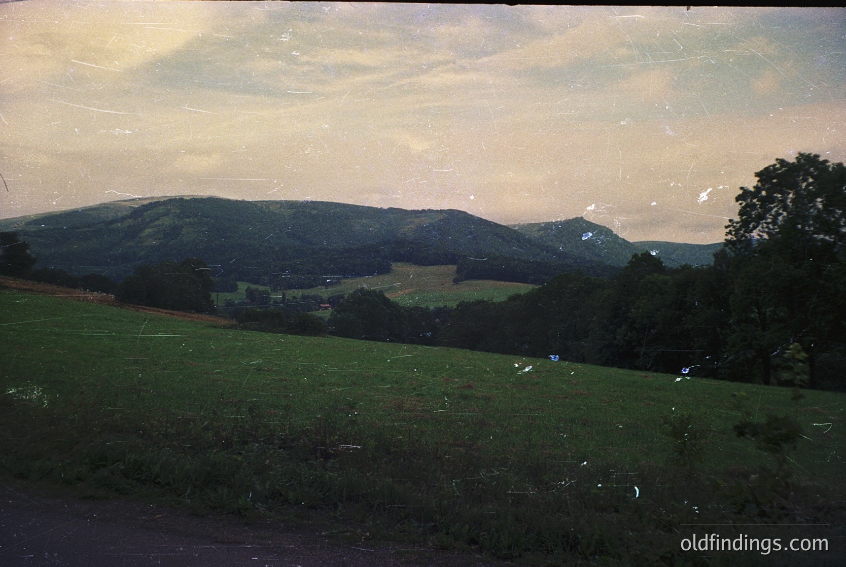 Vintage sepia-toned landscape featuring rolling hills and open fields under a hazy sky. Evidence of slight film damage and fading. Likely captured in the mid-20th century (1950s-1960s) for nostalgic or documentary use.