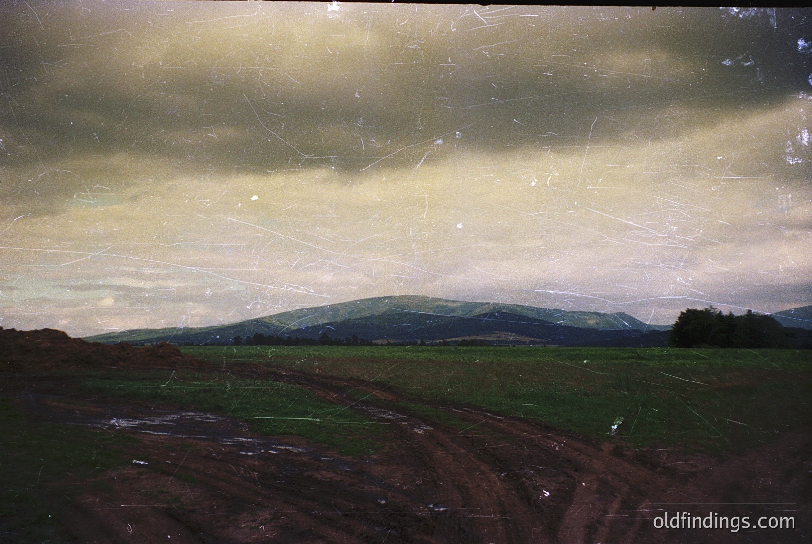 Vintage landscape photo showing rolling hills, farmland, and a cloudy sky. Evidence of aging film grain and scratches. Likely European countryside, mid-20th century.