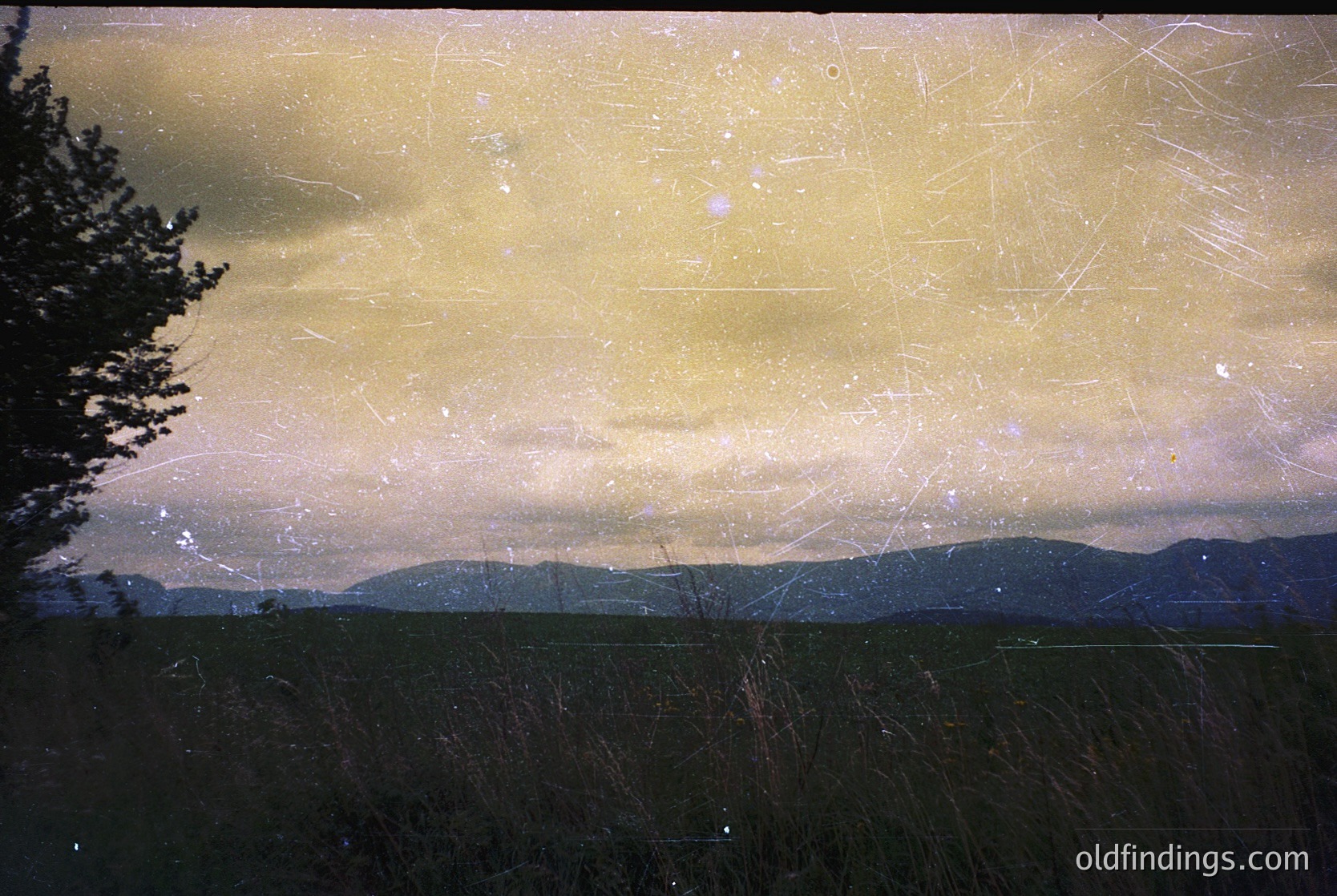 Vintage sepia-toned landscape shot through scratched film, revealing layered mountain ranges under overcast skies. Distorted textures and light leaks create abstract visuals. Likely 1970s–1990s analog photography.