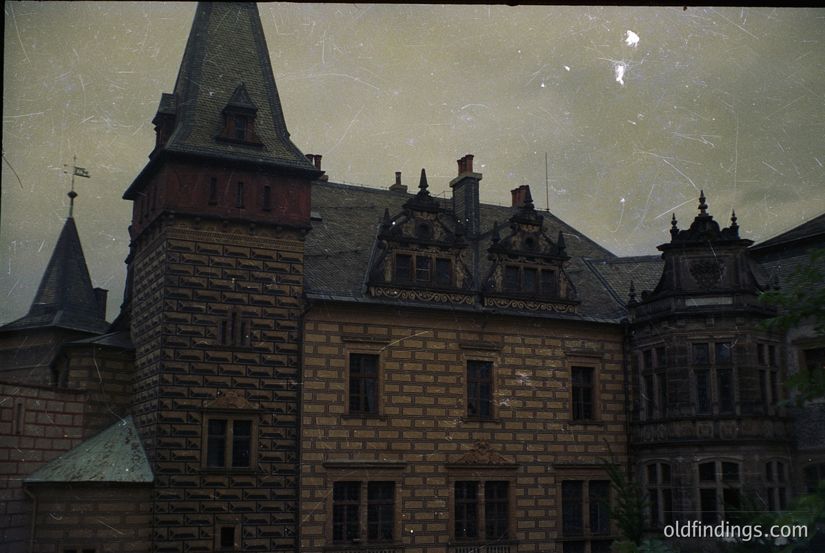 Vintage brick building with Gothic Revival architecture—steep gables, ornate dormer windows, and a corner turret. Yellowed, scratched film grain suggests mid-20th century. Likely European institutional or residential structure.