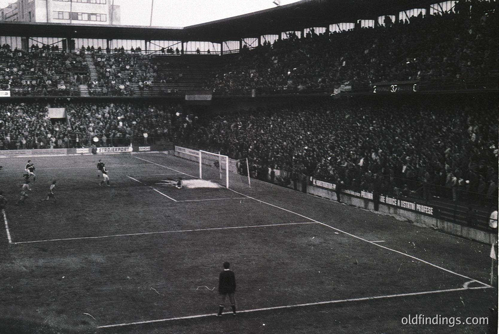 Black-and-white shot of a packed stadium during a mid-20th-century football match, likely 1950s–1960s. Crowds fill tiered stands, with players in action near the goal. Advertising banners (e.g., "Coca-Cola") and a referee in traditional attire visible. Iconic midfield perspective captures the scale of early stadium design.