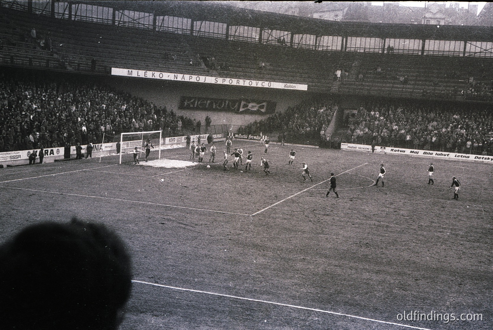 Black-and-white soccer match in a packed stadium, featuring a crowded stands with spectators and banners reading "Mesto Naro Sportu" and "Xenon." Players in vintage uniforms engage in action near the goal. Mid-20th century European football atmosphere. Ideal for sports history or vintage sports research.