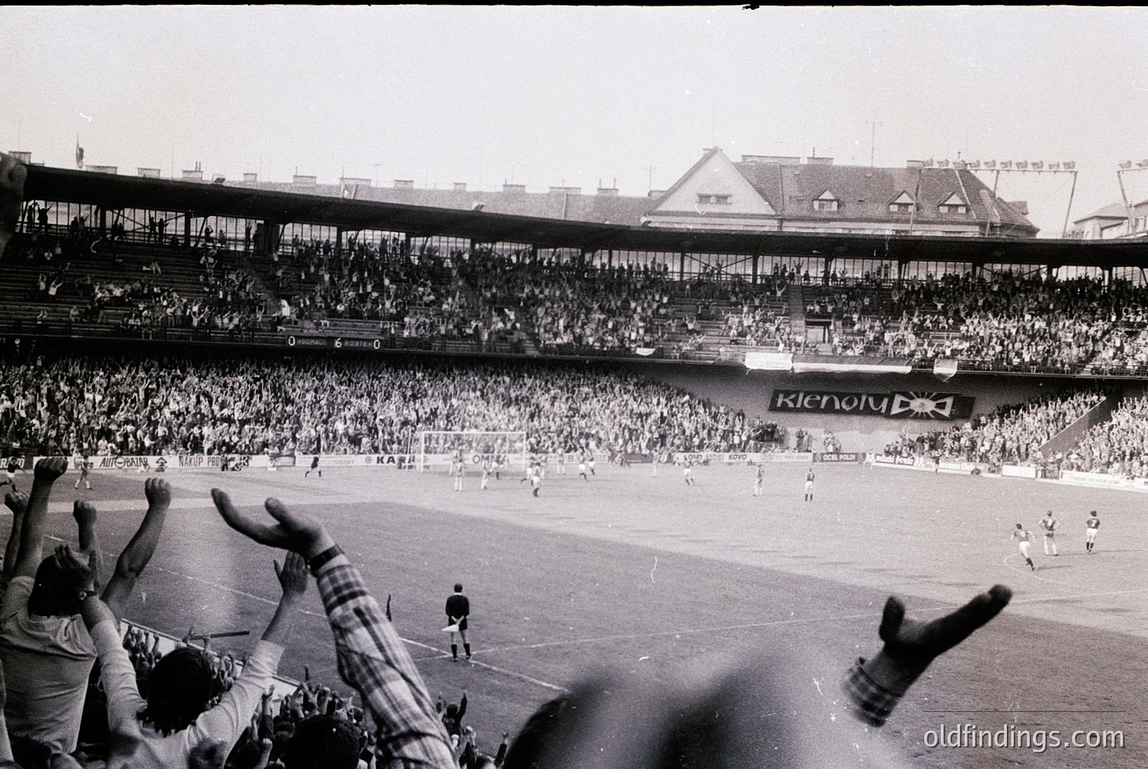 Vintage black-and-white stadium shot showing packed stands with spectators raising arms in celebration. Prominent "Renault" advertisement on the side. Mid-20th century European football match atmosphere. Crowded, multi-tiered seating with classic architectural details.